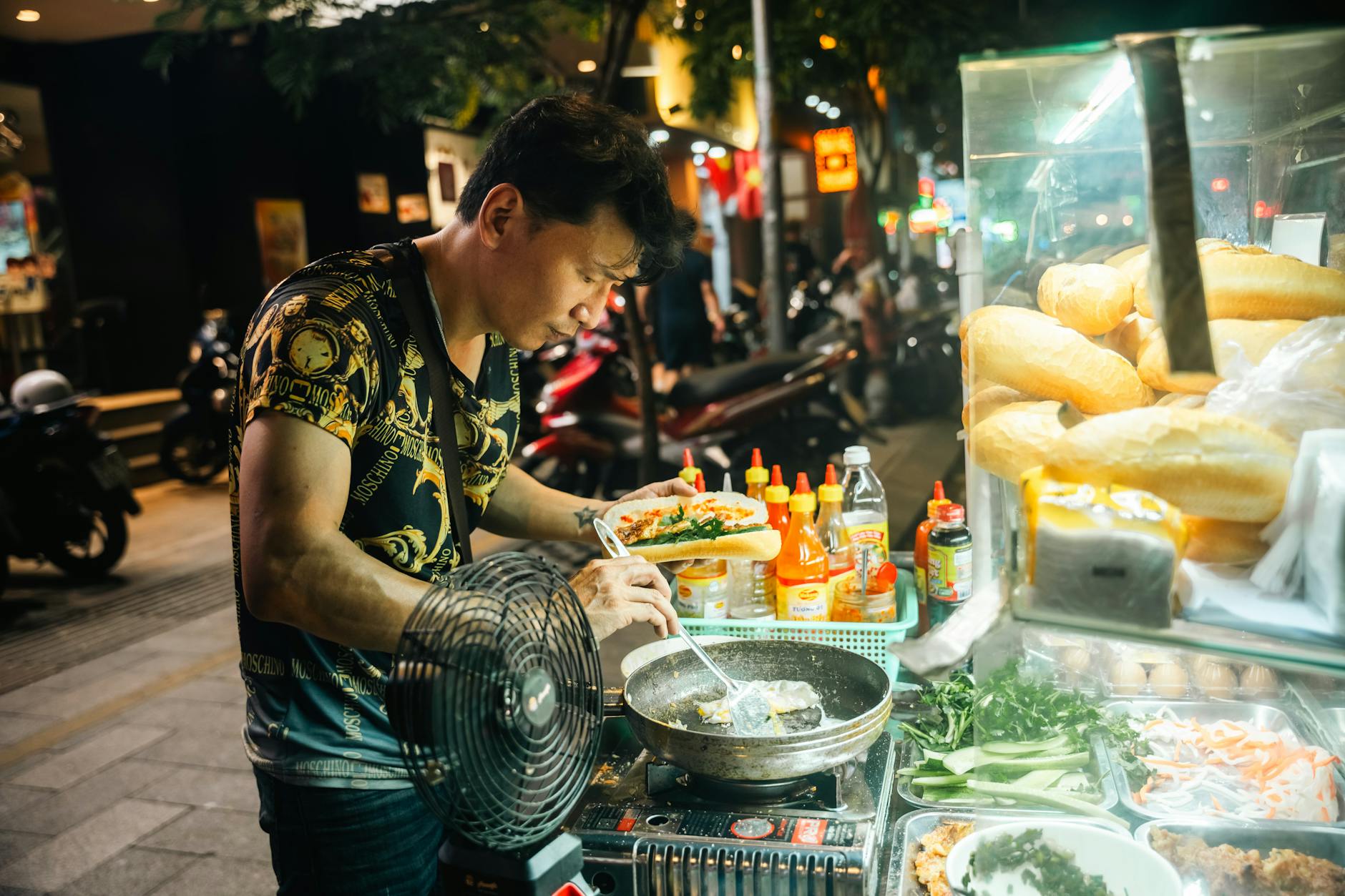 A street food vendor cooks and assembles Vietnamese banh mi at a bustling night market.