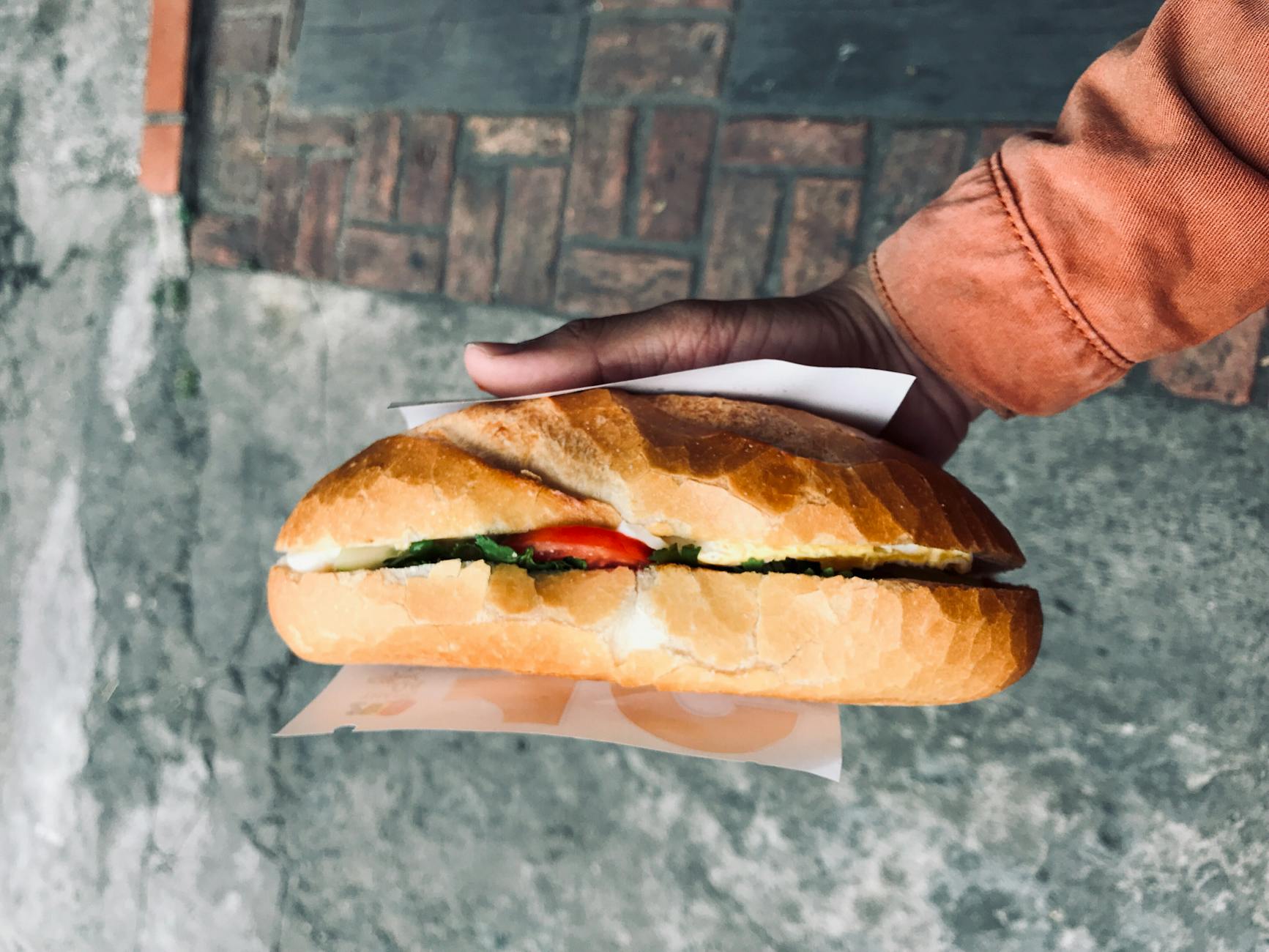 Close-up of a traditional Vietnamese banh mi sandwich held over a street pavement in Hue City, Vietnam.