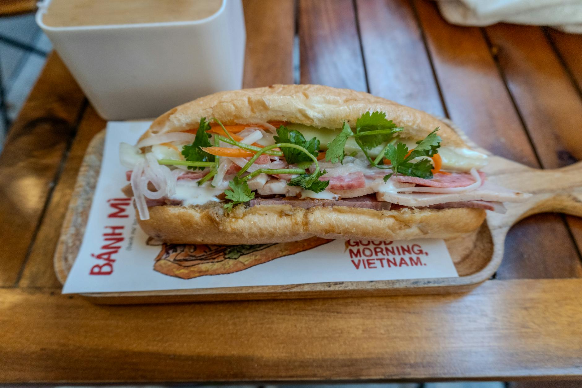 Close-up of a fresh and vibrant Vietnamese Bánh Mì sandwich served with a message saying 'Good Morning, Vietnam'.