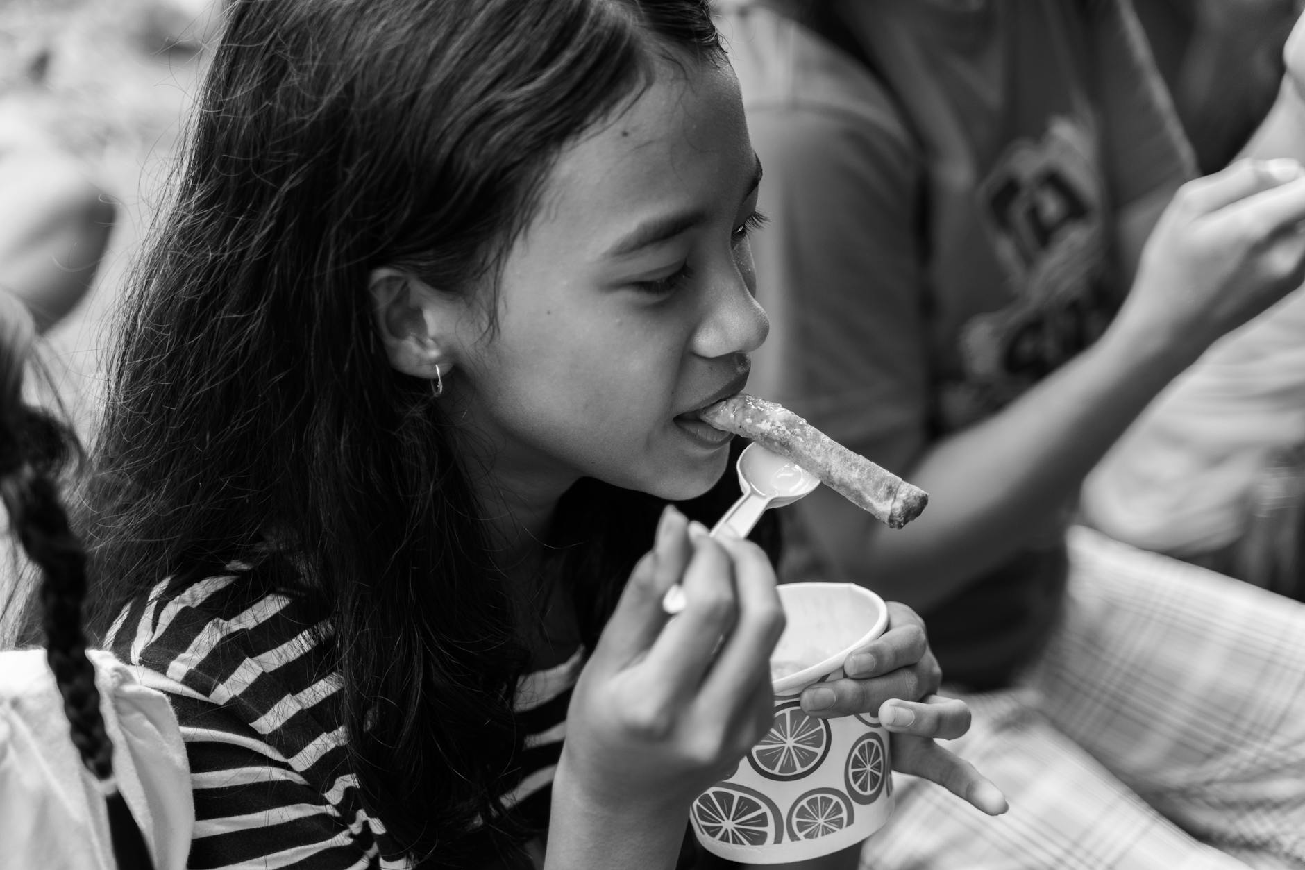 A young girl enjoys a snack in a candid black and white photograph.