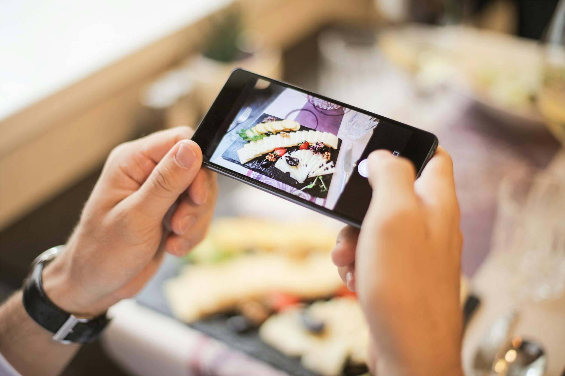 Hands holding a smartphone capturing a photo of a plated dish in a cozy setting.