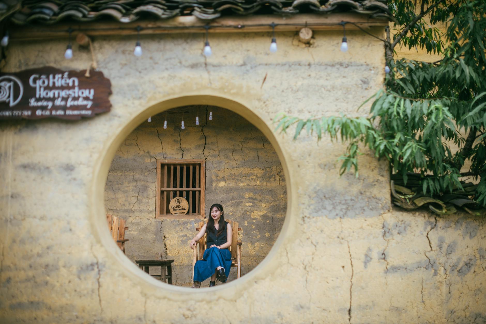 A woman seated in a rustic homestay capturing the essence of traditional architecture.