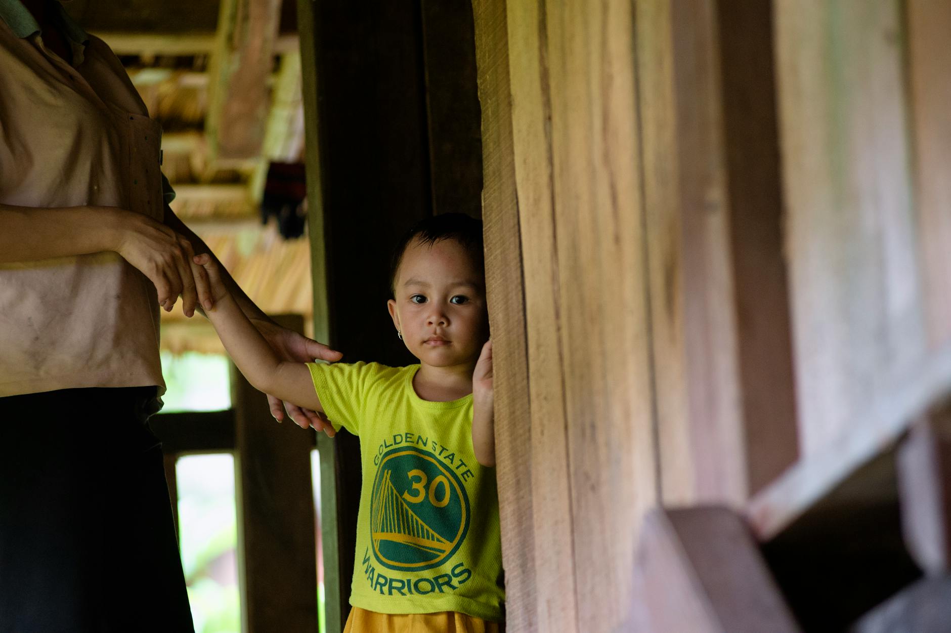 A young boy in a bright shirt stands in a traditional wooden house in Hà Giang, Vietnam.