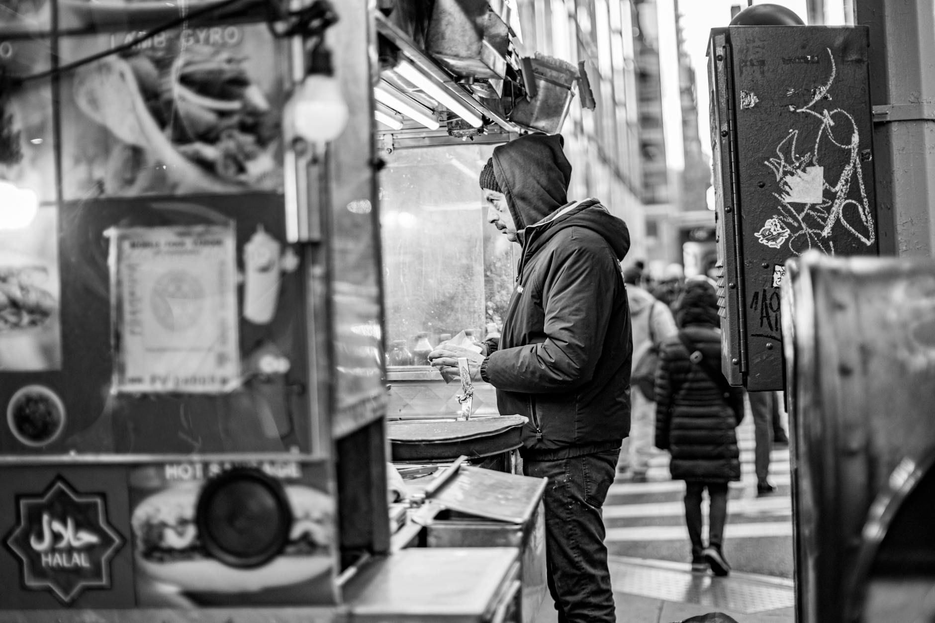 Black and white photo of a street vendor serving food in New York City.