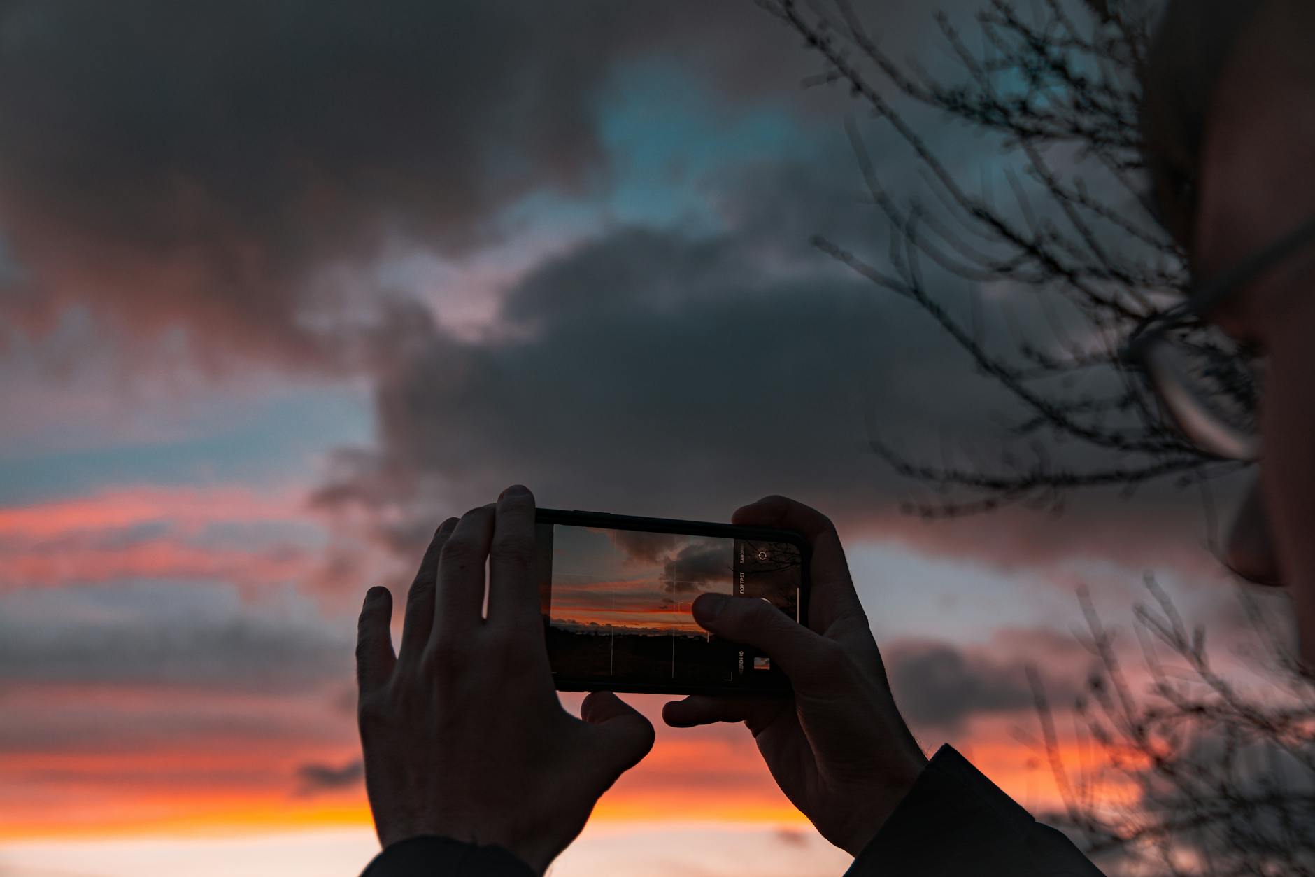 Silhouette of a person capturing a vibrant sunset with a smartphone in hand.