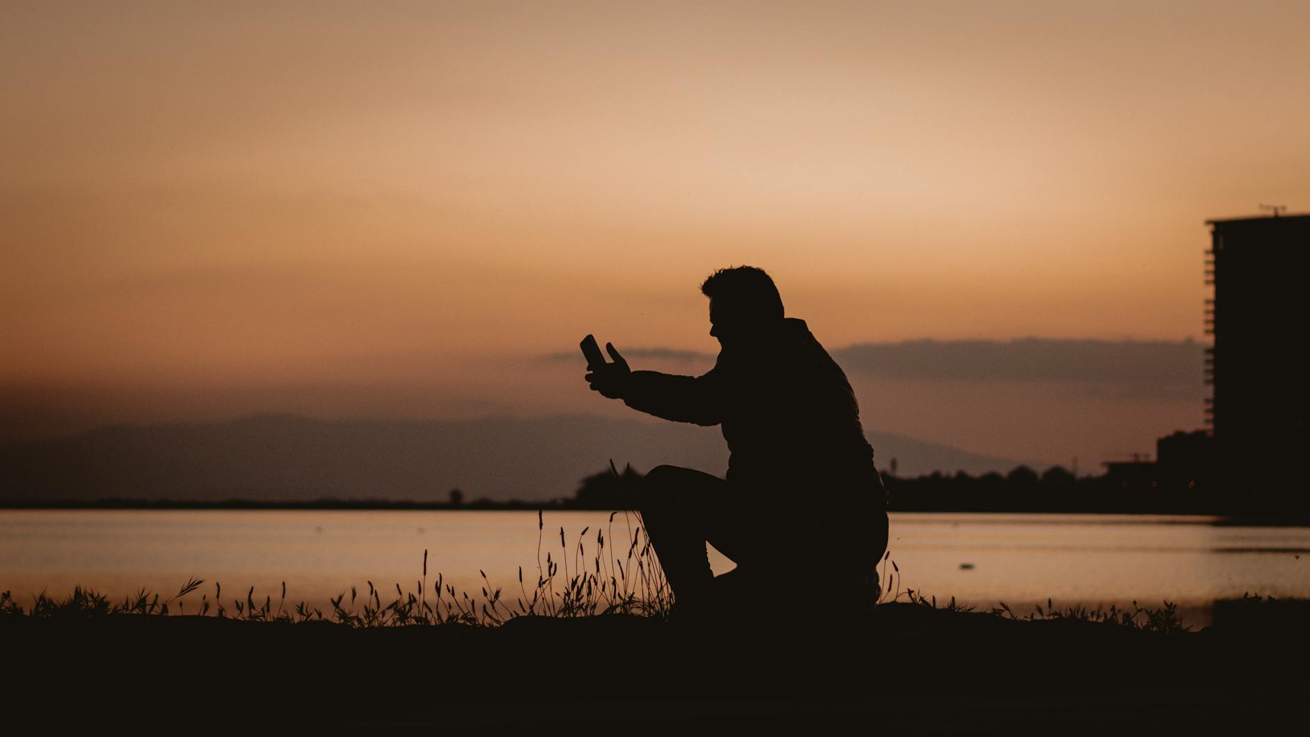 Silhouette of a person capturing a sunset by the water in Amsterdam with a smartphone.