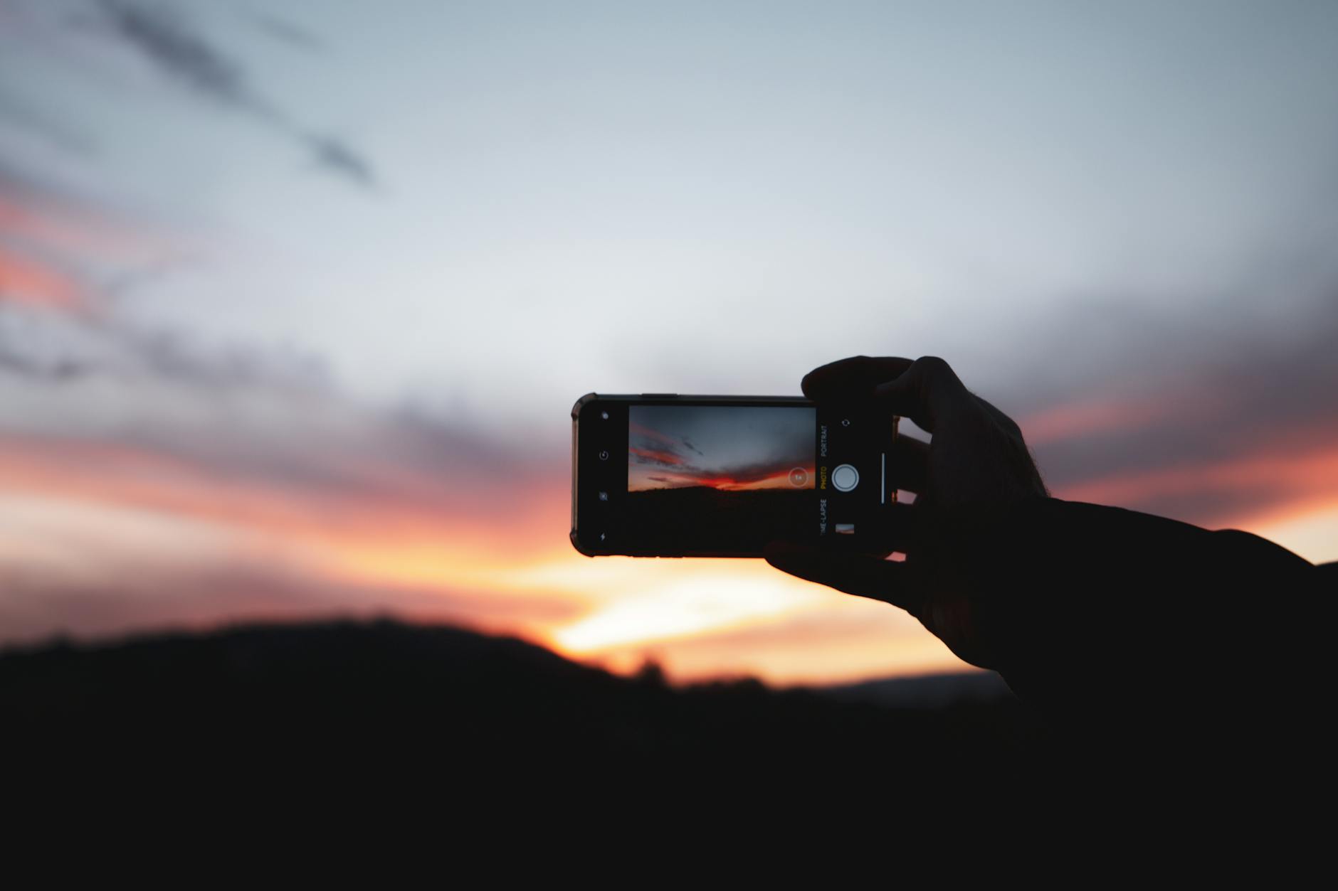 Person holds smartphone to capture vibrant sunset sky. Perfect for technology and nature themes.