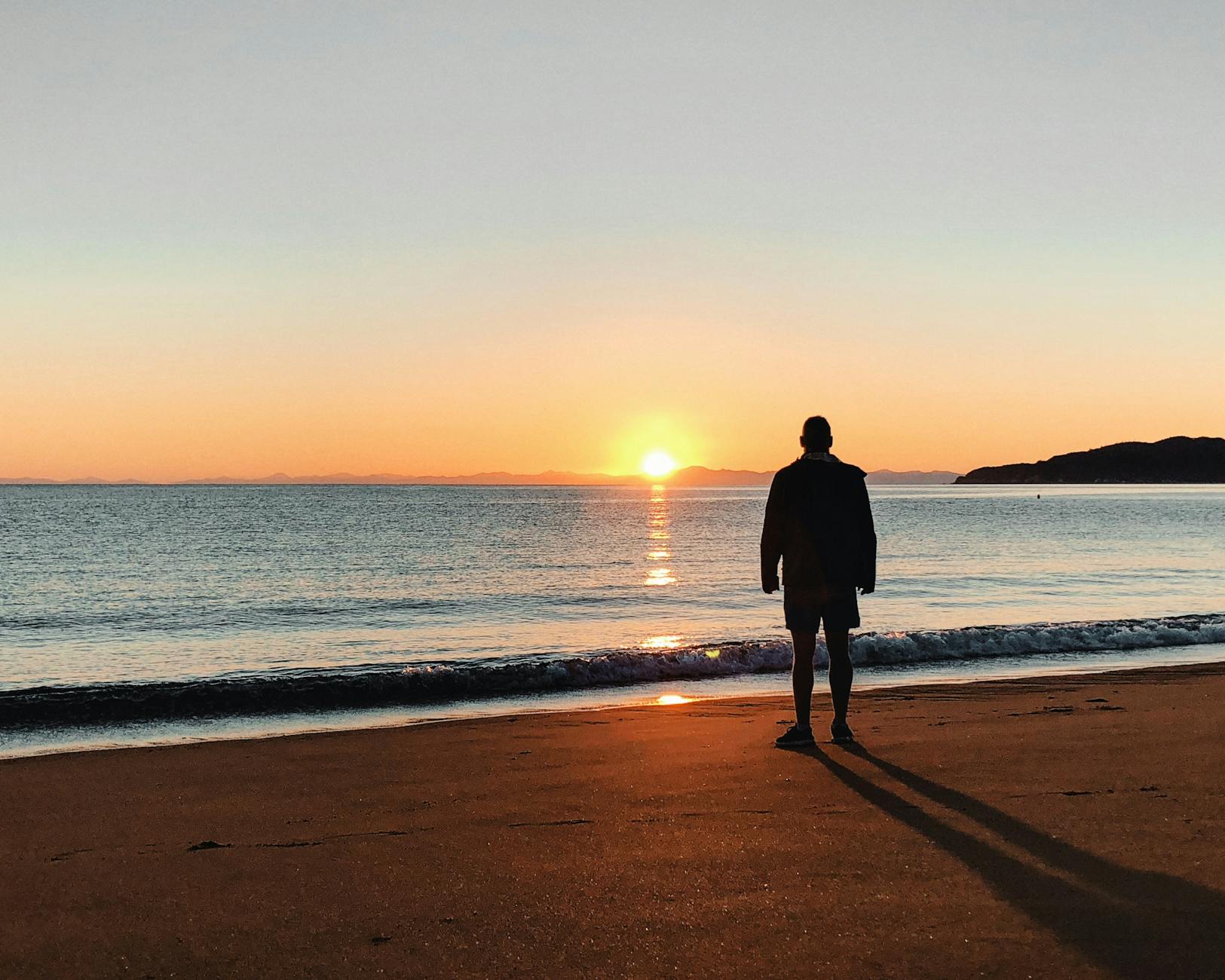 Silhouette of a person on a beach during a vibrant sunrise, capturing peace and solitude.
