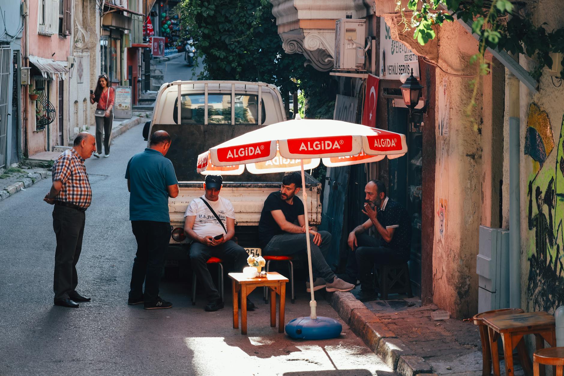 Casual street scene of a group of men relaxing under an Algida umbrella in Istanbul.