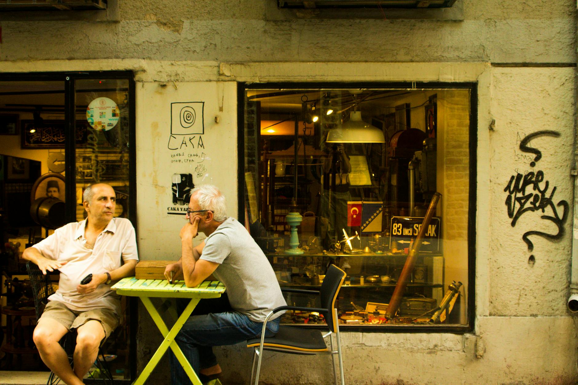 Two men engage in conversation at a street cafe in the city with vintage decor and urban graffiti.