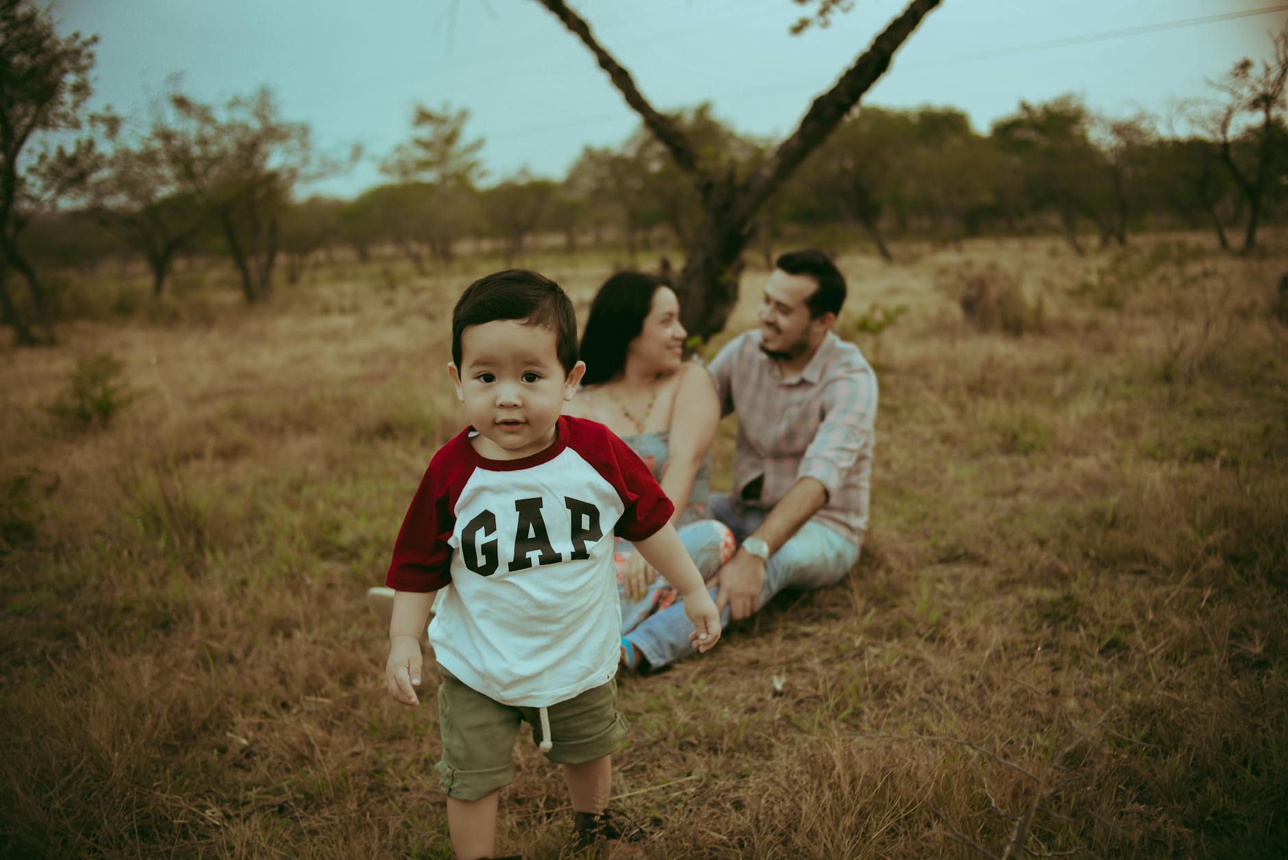 Happy family sitting in a field with son walking towards the camera in Mexico.