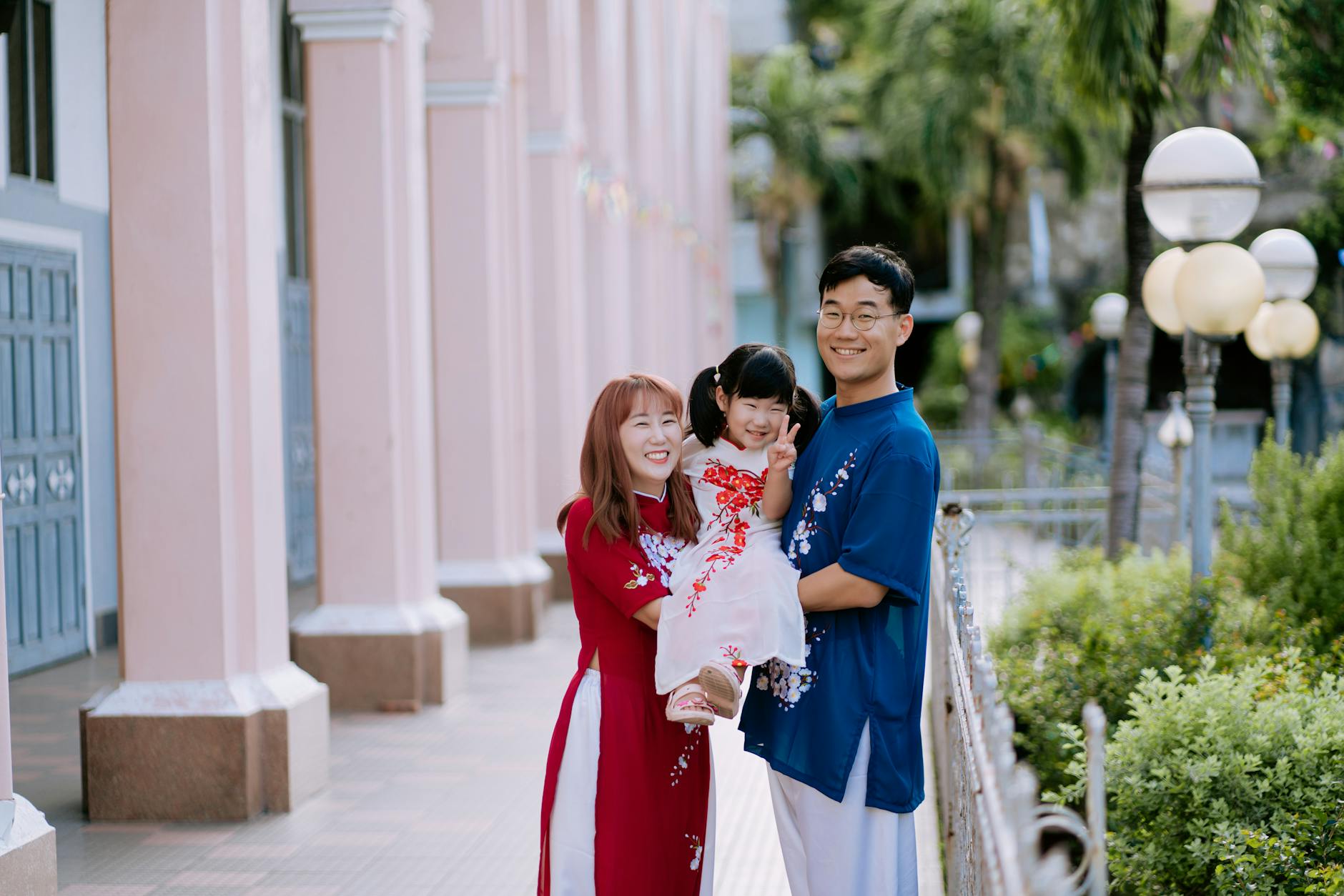 Smiling Asian family in traditional ao dai, enjoying a sunny day outdoors.