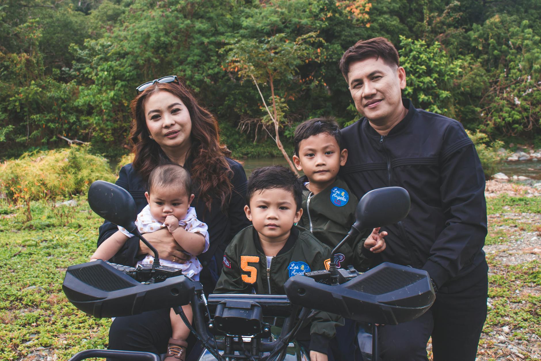 A family of five outdoors posing with a motorcycle in a lush green meadow.