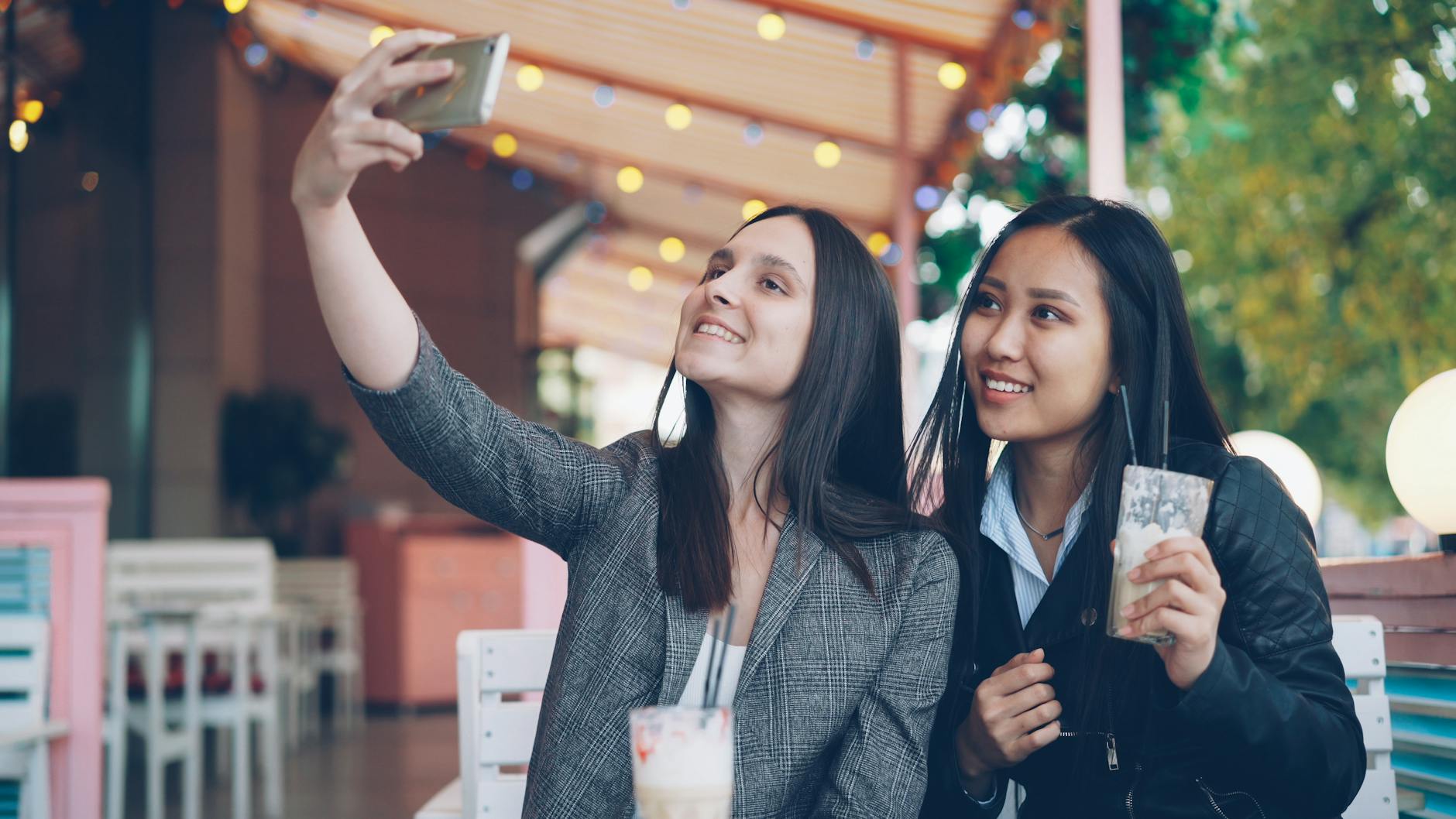 Two young women having coffee and taking a selfie at an outdoor café.
