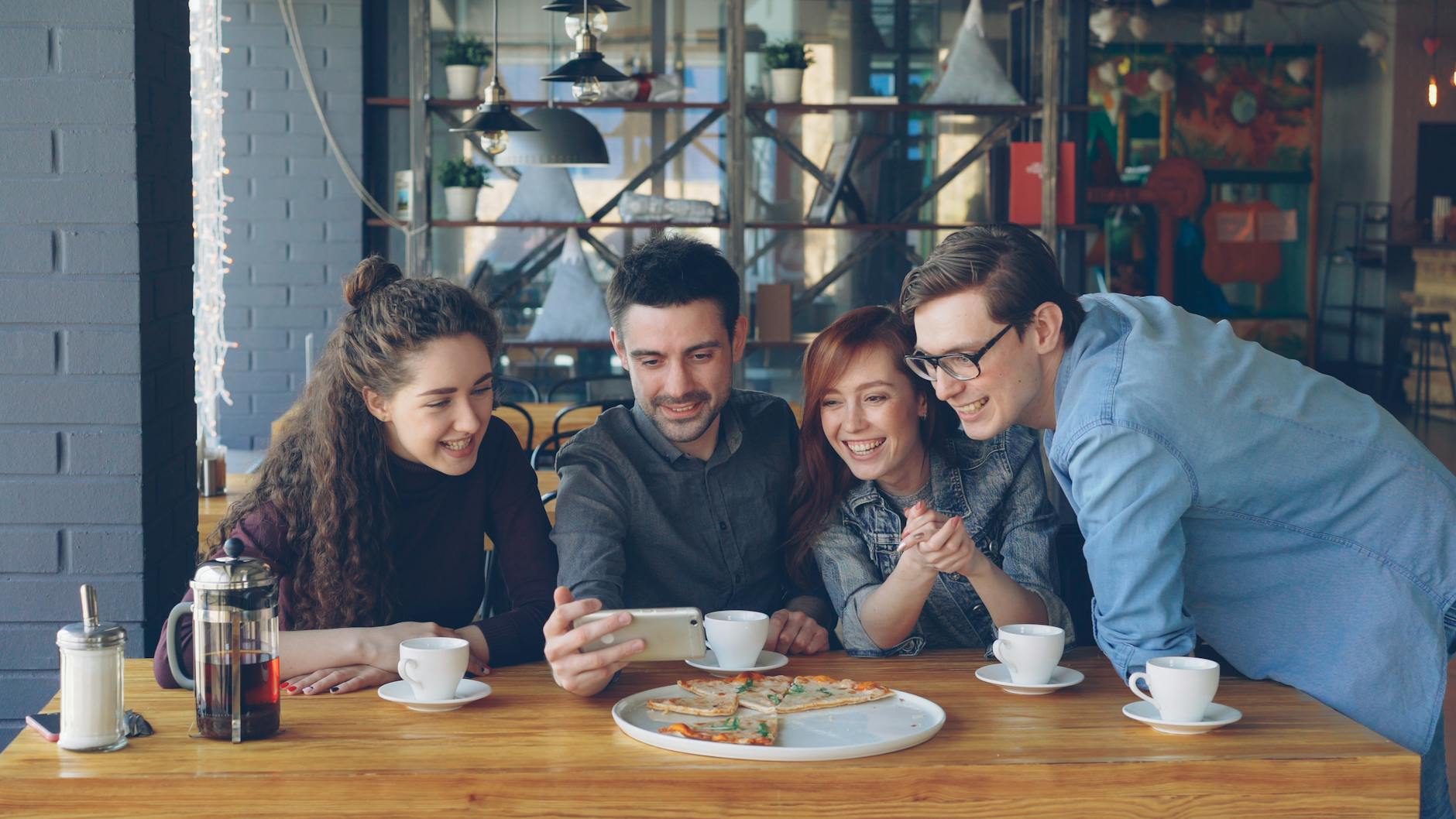 Four friends share a fun moment over coffee and pizza in a cozy cafe.