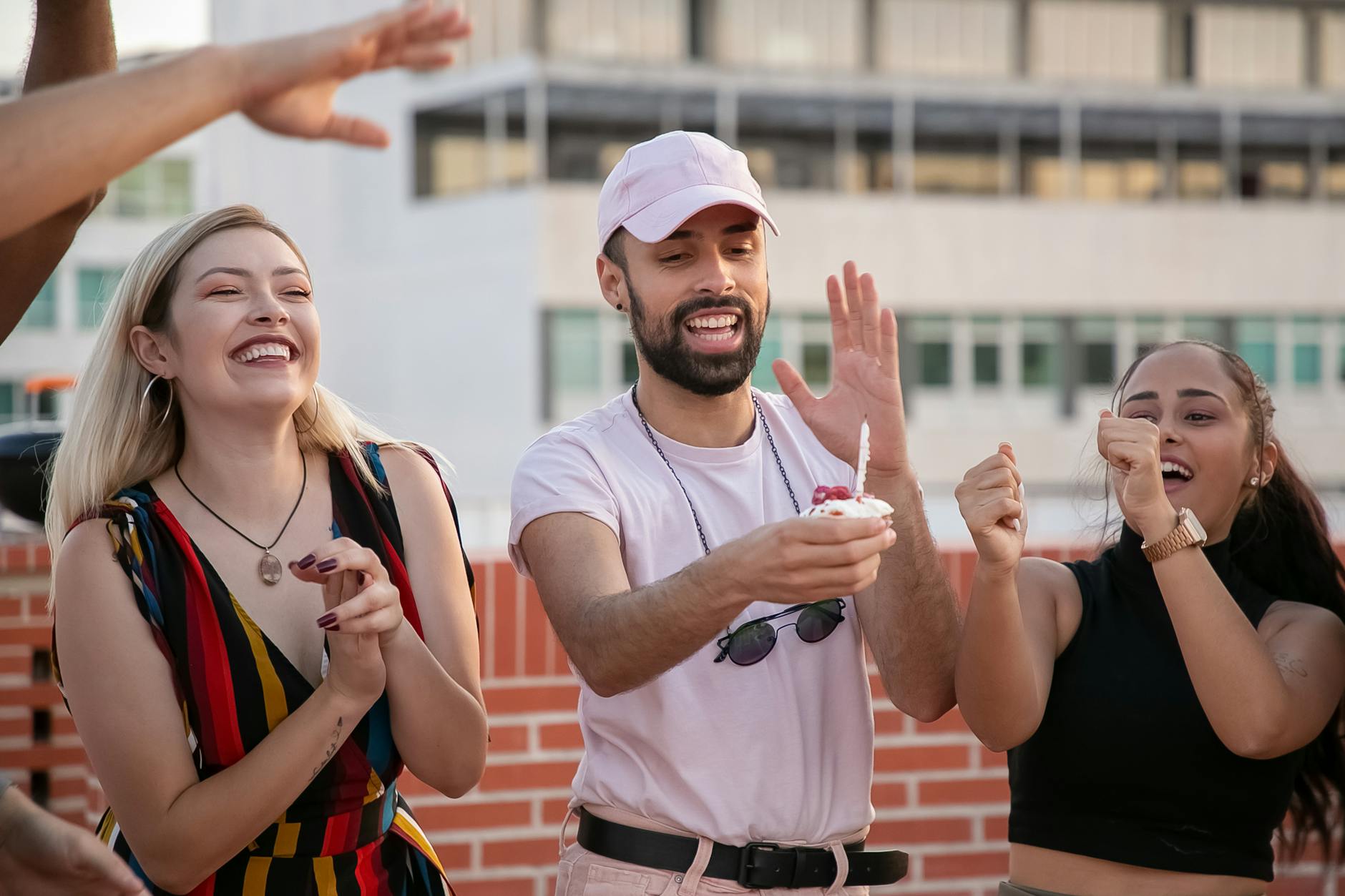 Group of friends celebrating with a cupcake on a sunny rooftop, capturing joyful moments.