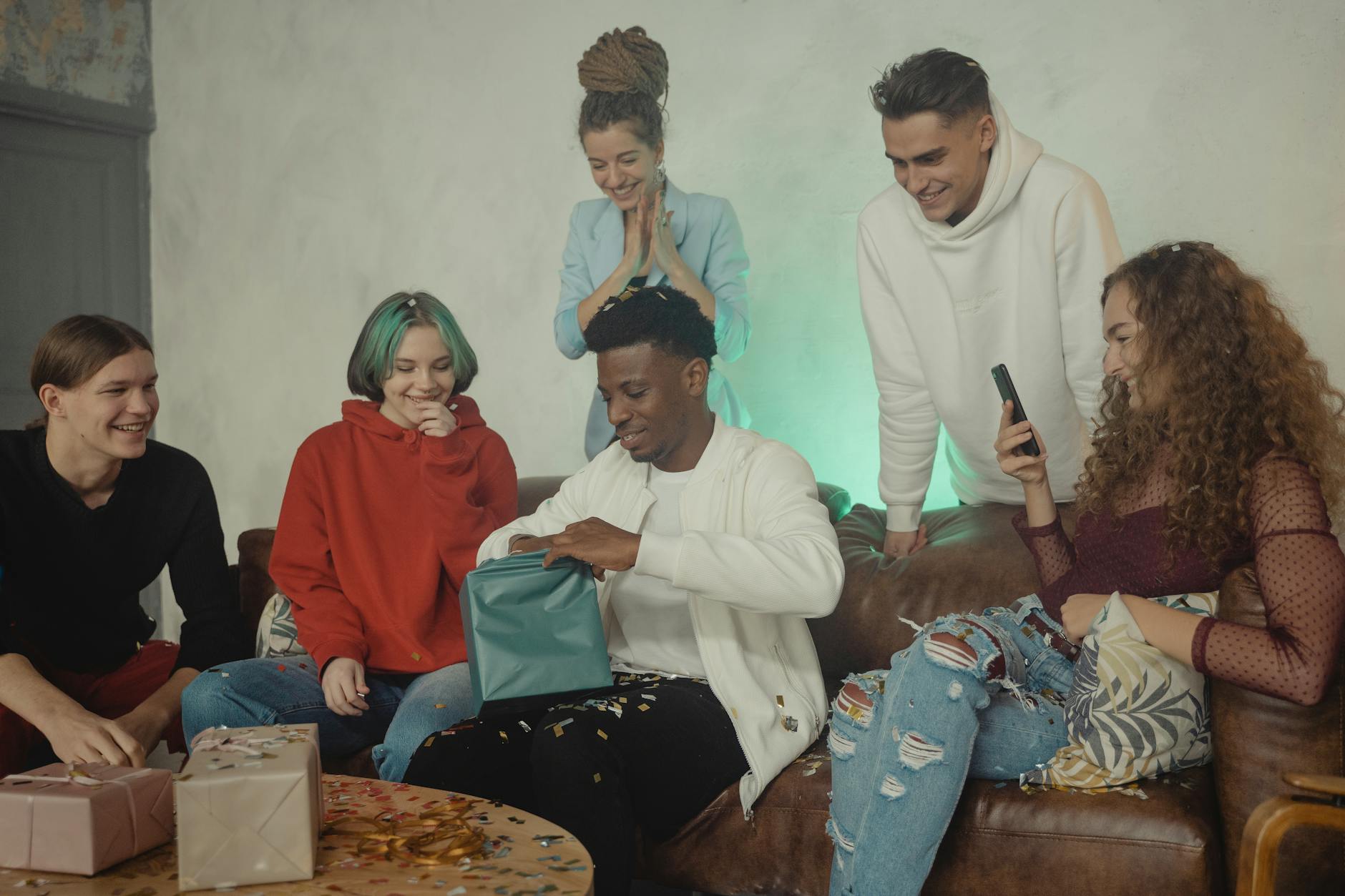 A group of friends celebrating a birthday opening presents indoors, showcasing diversity and camaraderie.