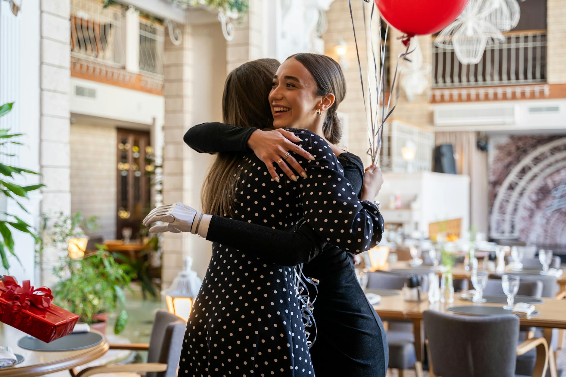 Two women warmly embrace in a festive indoor setting, highlighting friendship and joy.