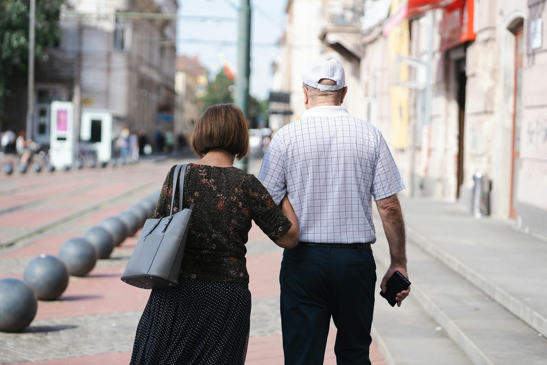 Senior couple walking arm-in-arm on a sunny urban street, capturing a moment of togetherness.