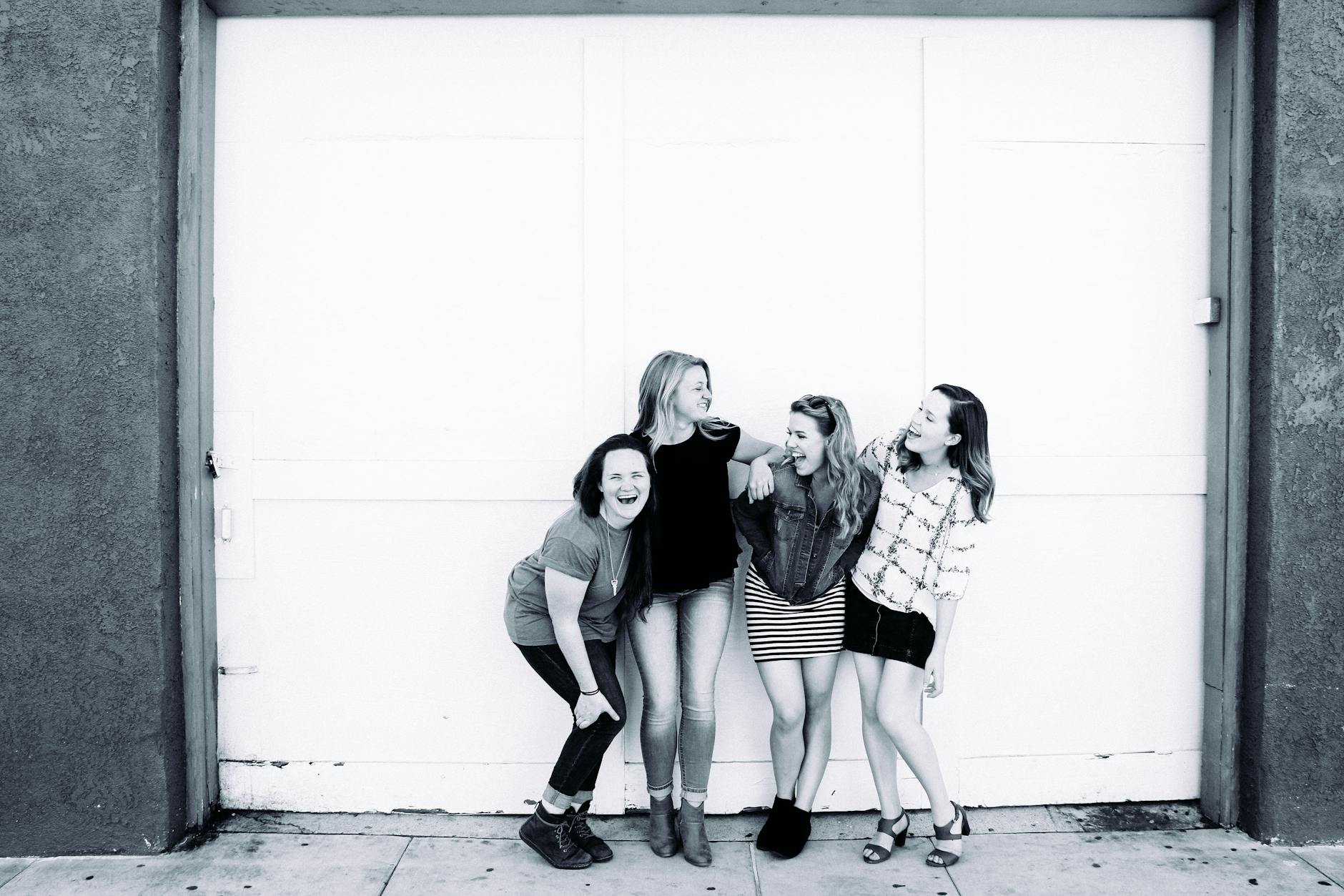 Four young women laughing together in front of an urban door, showcasing friendship and happiness.