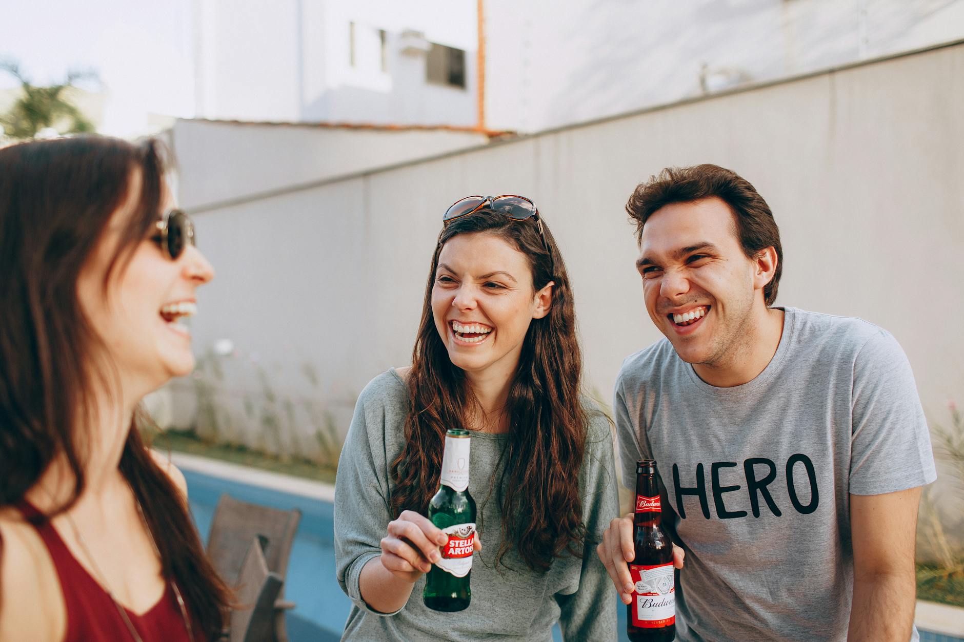 Three friends laughing and enjoying drinks outdoors, sharing happy moments.