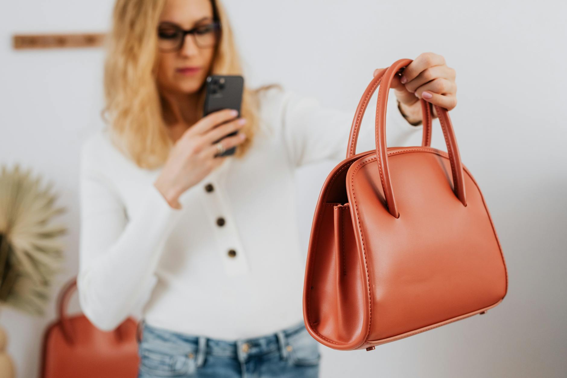 Caucasian woman photographing a fashionable handbag with a smartphone for online selling.