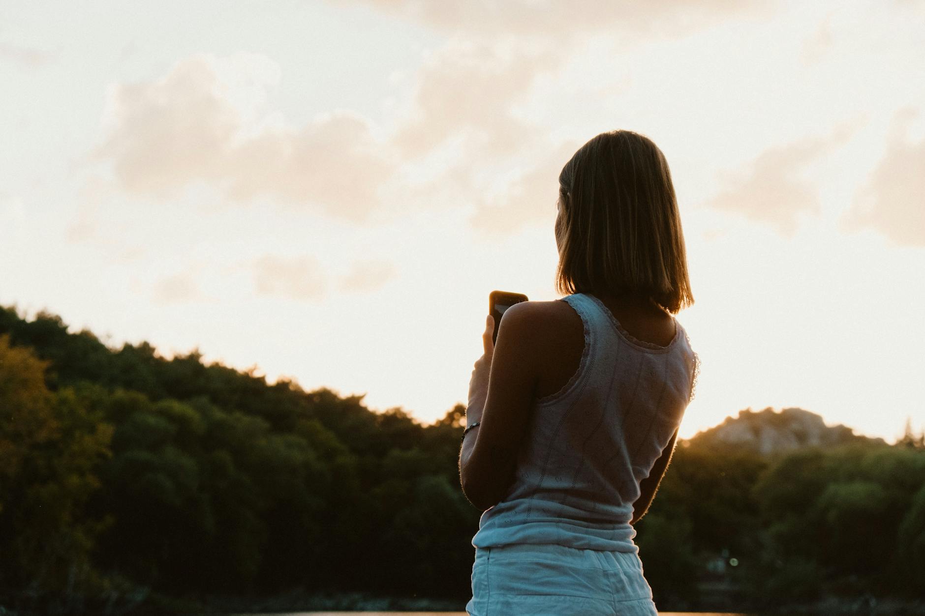 A woman with short hair captures a breathtaking sunset using her phone.