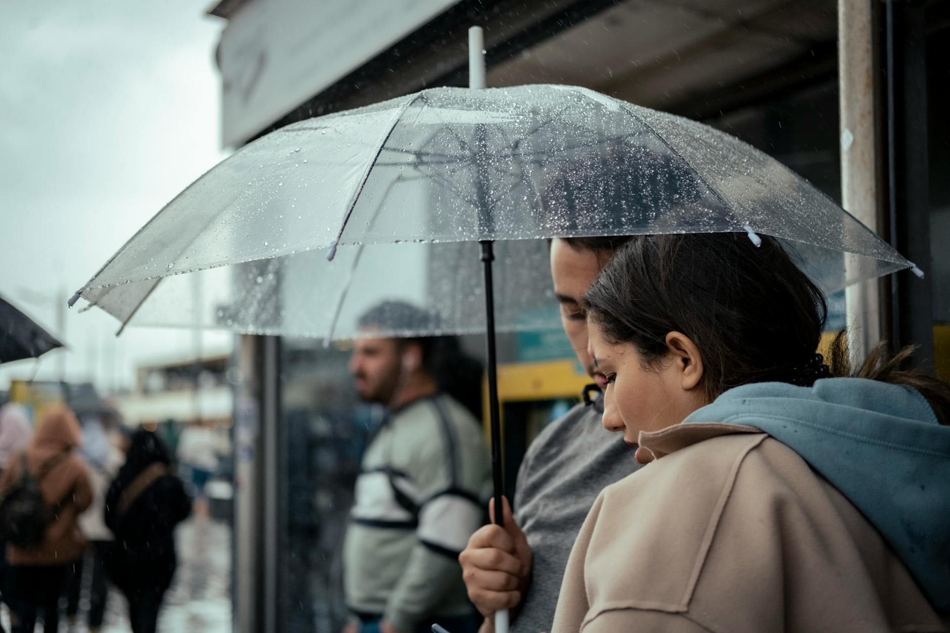 A candid moment of a couple sharing an umbrella in a busy, rainy city street.
