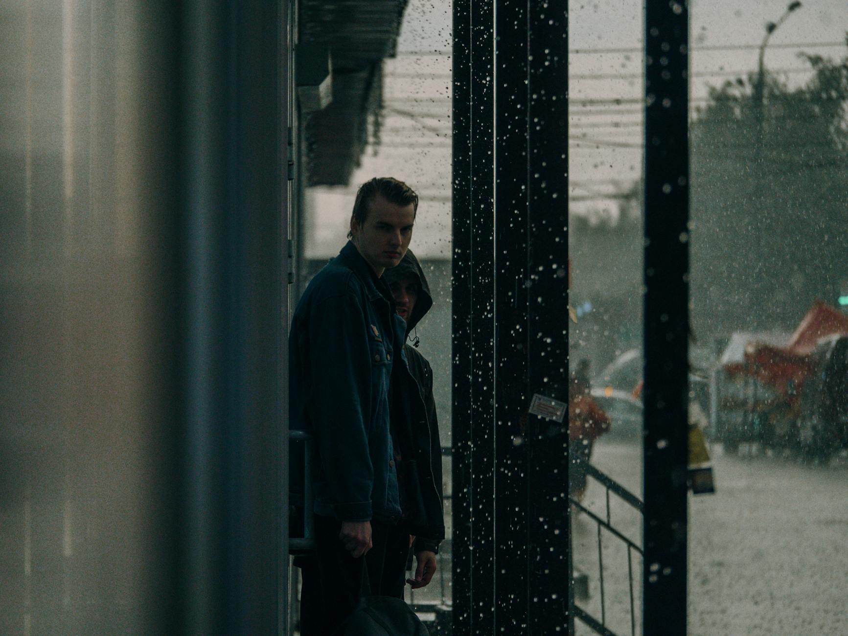 A moody scene of men waiting at a bus stop in the rain, showing emotion and atmosphere.