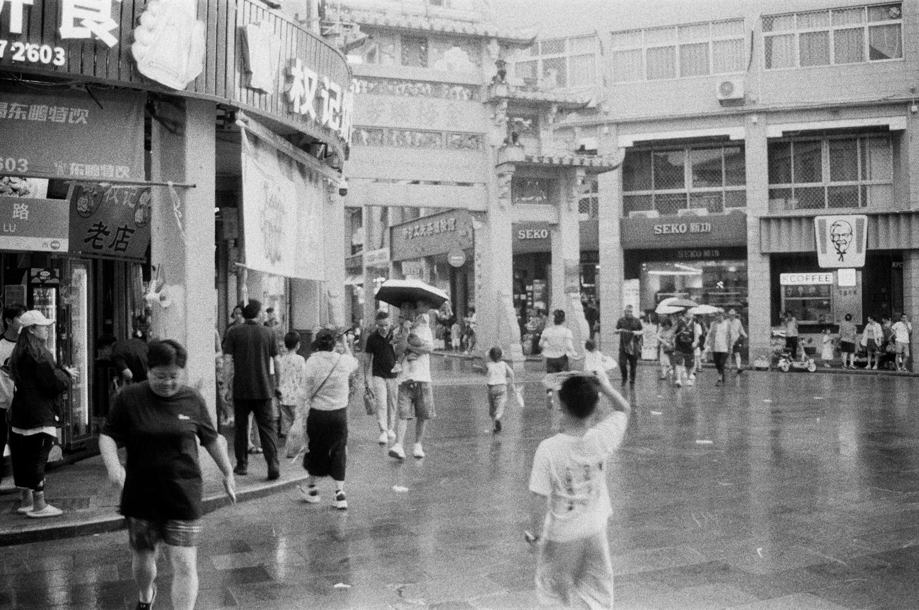 A bustling scene of a historic Chinese market street in black and white with people shopping and exploring.