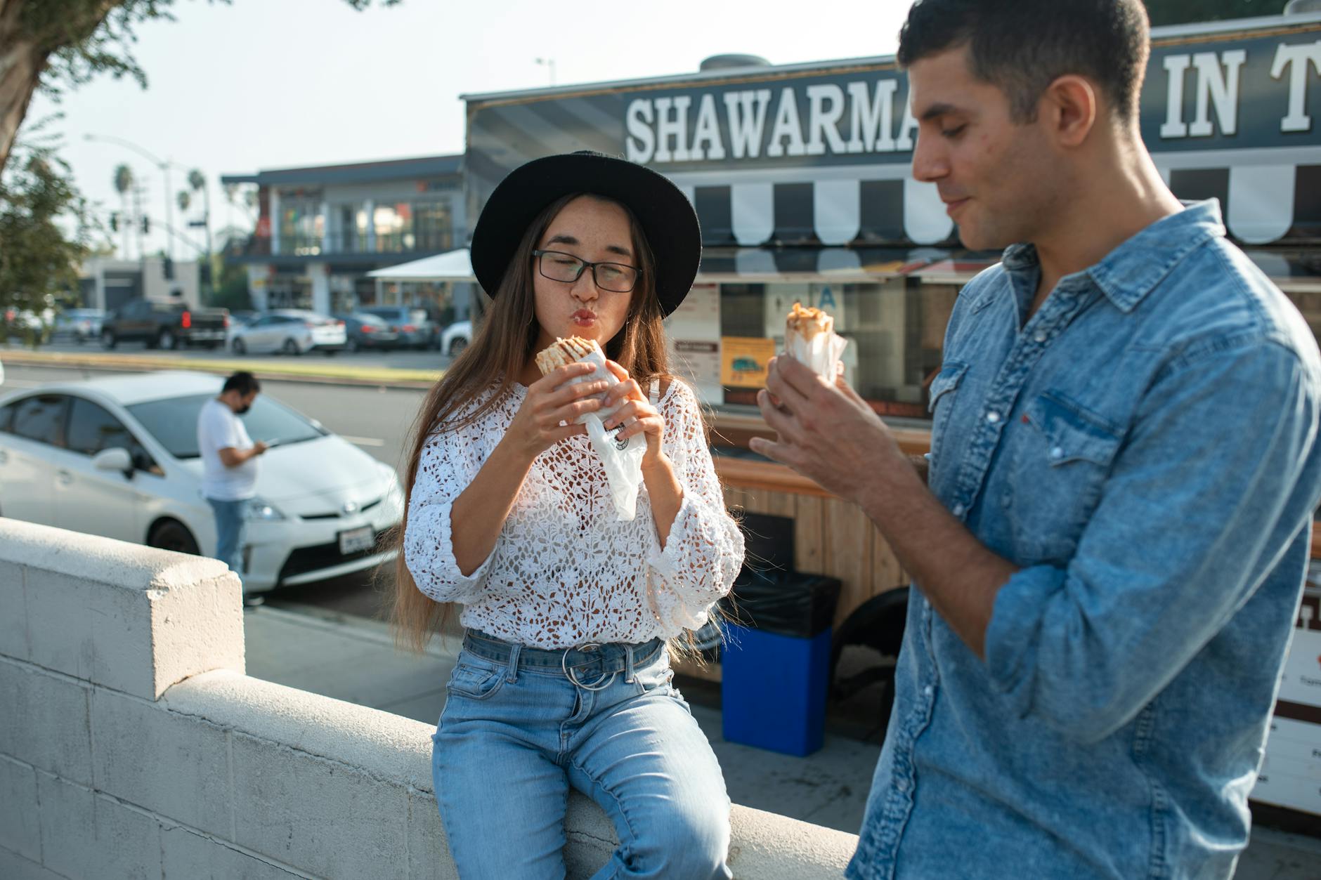 Two friends savor shawarma while enjoying the sunny outdoors, showcasing casual leisure and street food culture.