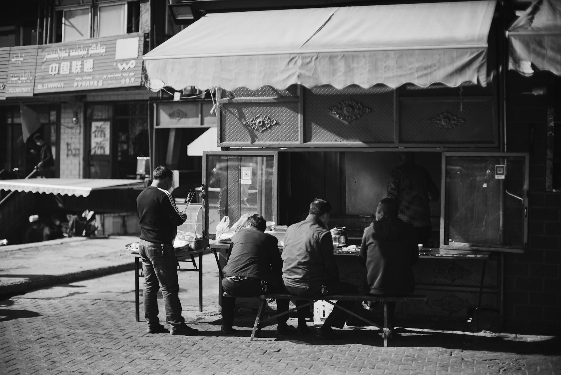 A candid black and white photo of people enjoying street food at an outdoor market.