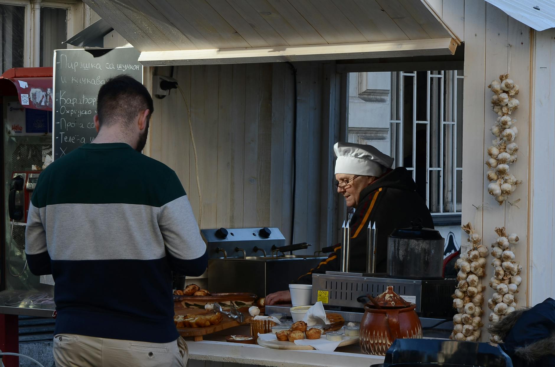 Street vendor at an outdoor market serving food with display of garlic strings.