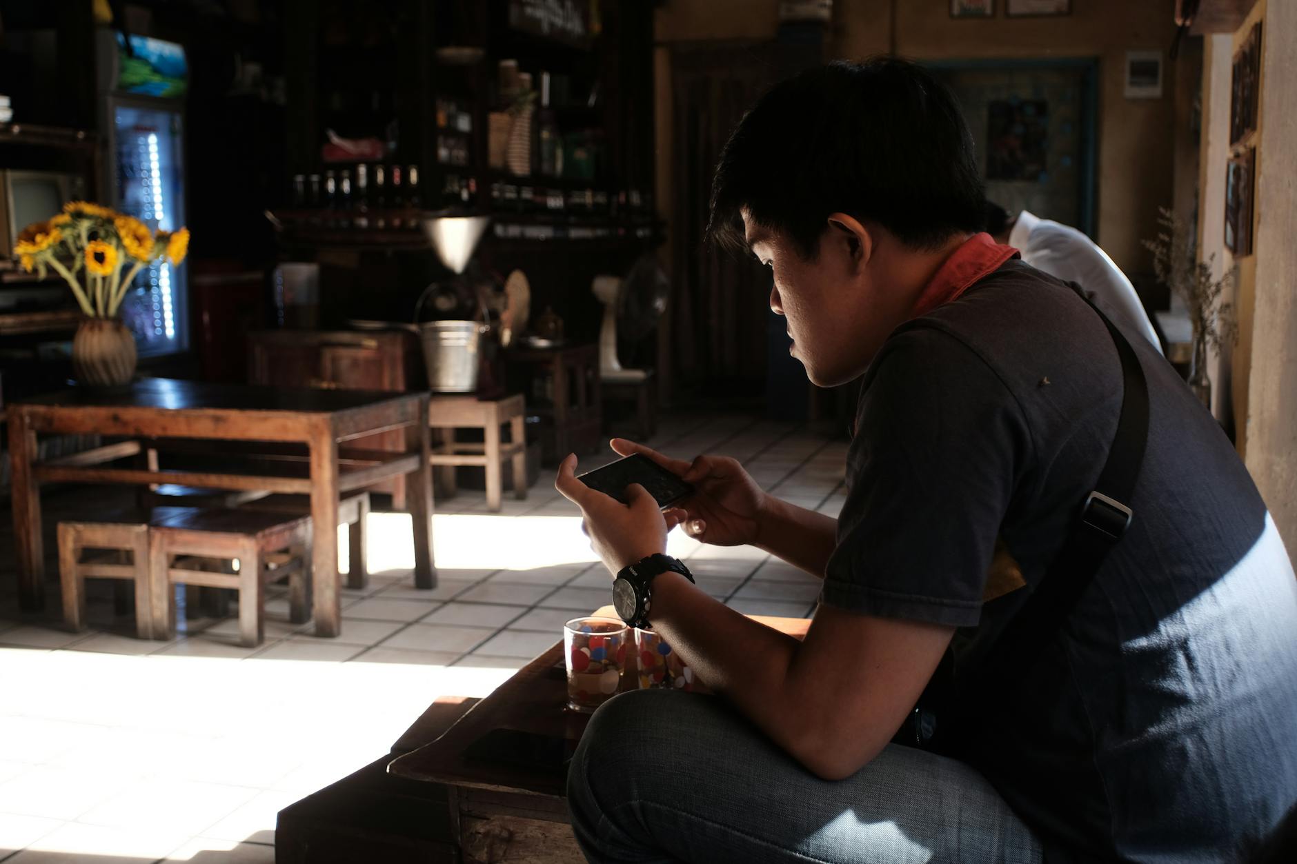 Man sitting indoors using smartphone in a rustic cafe, enjoying the tranquil atmosphere.