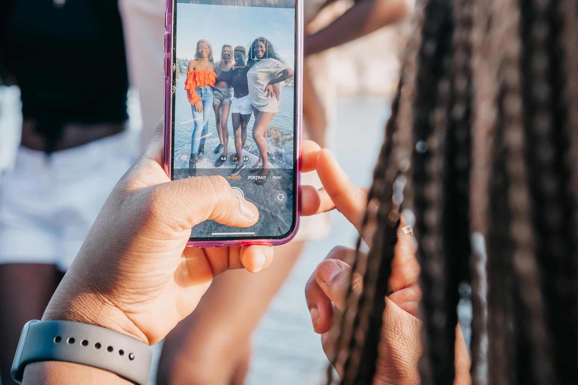 Group of friends taking a photo with a smartphone during a sunny day outdoors.