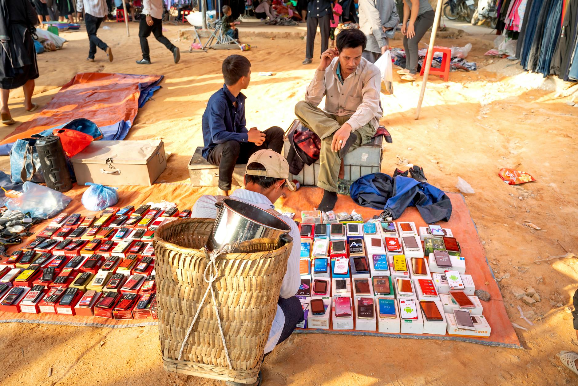 From above of anonymous ethnic male locals sitting on chairs on sandy ground and selling various smartphones on bazaar