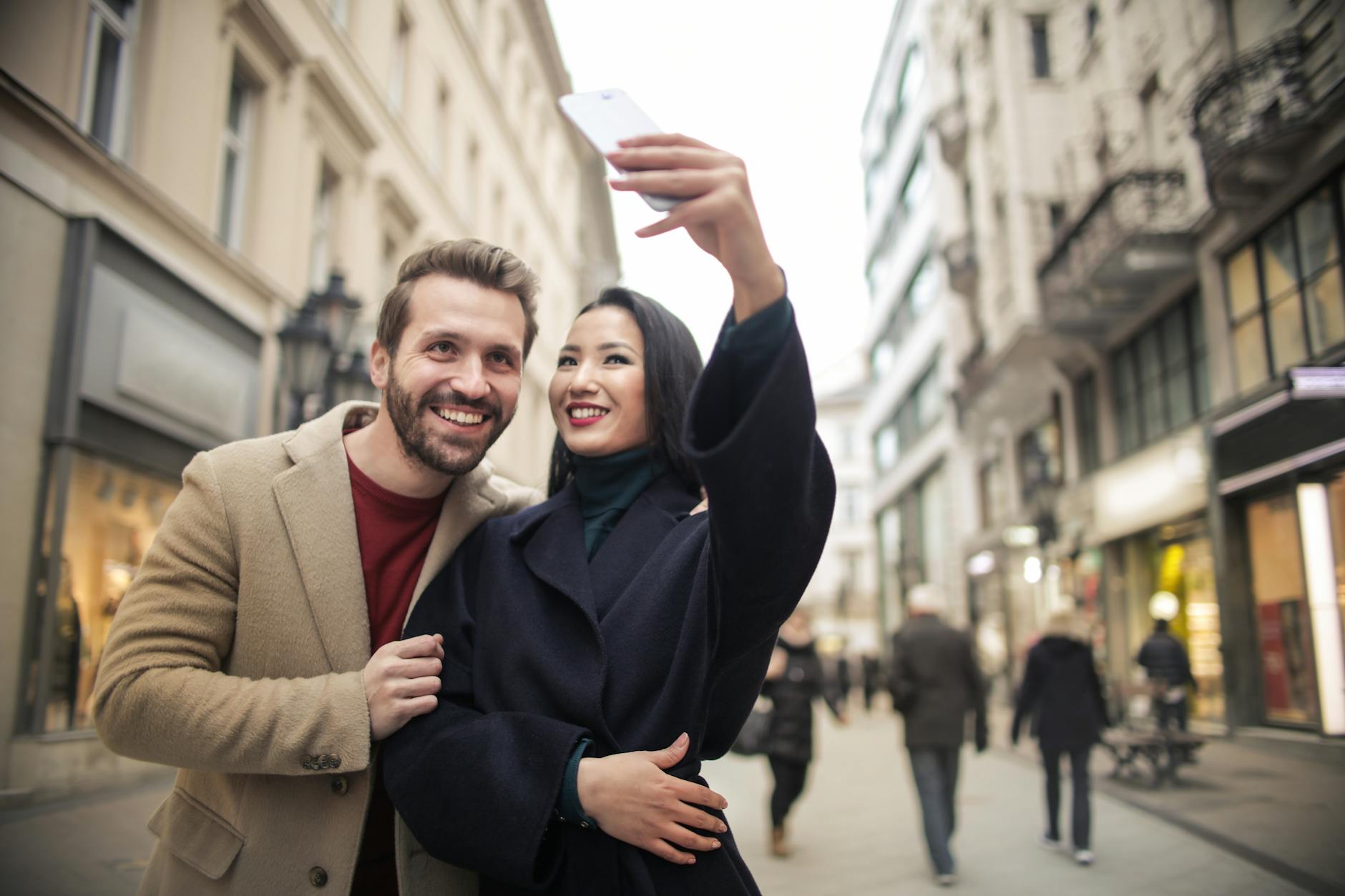 Happy couple takes a selfie on a lively urban street in daylight, capturing joyful moments during their city walk.