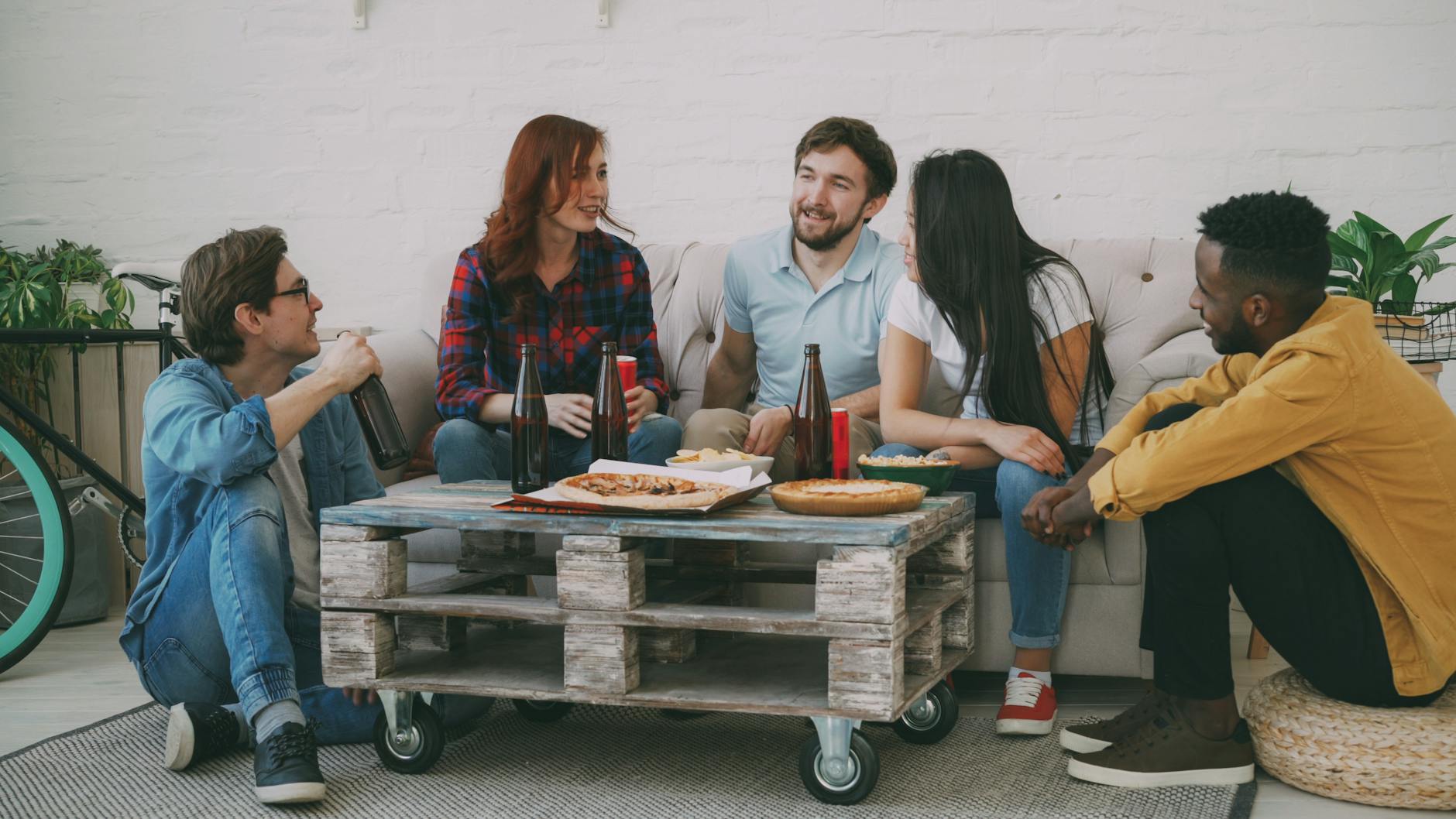 Group of friends sharing pizza and drinks at home, enjoying casual conversation.