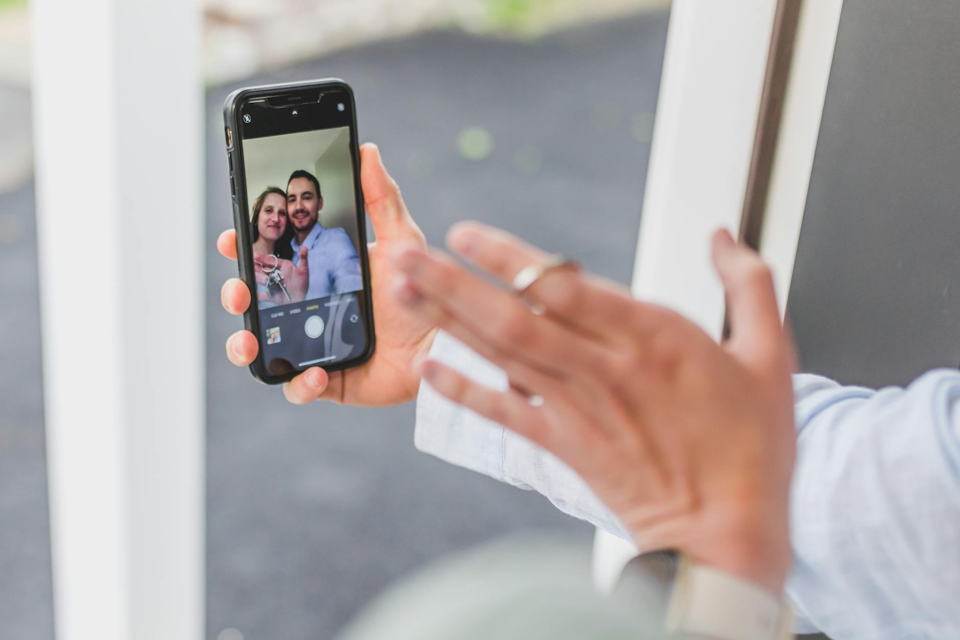 Close-up of hands holding a smartphone showing a couple taking a selfie outdoors.