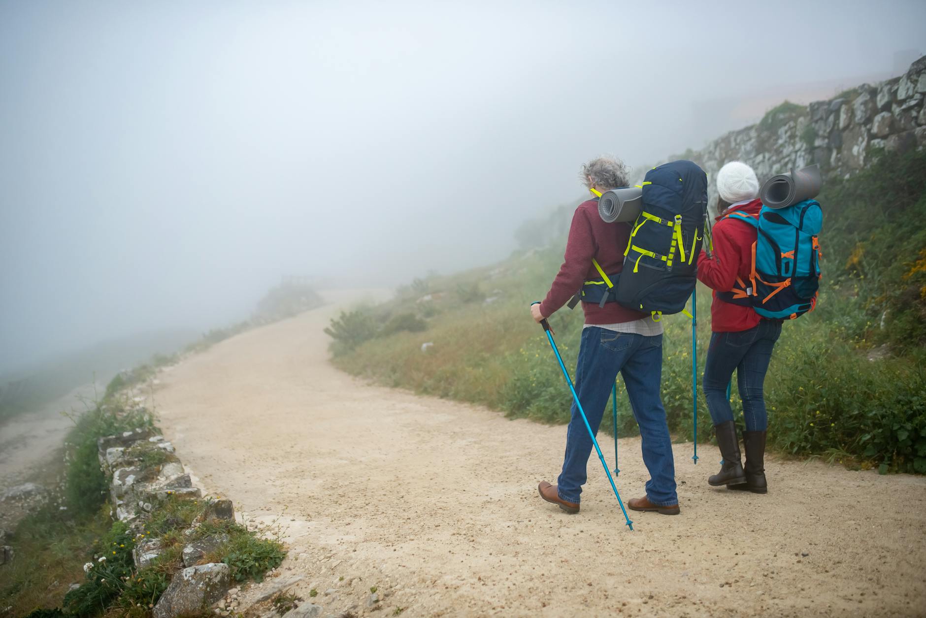 Couple hiking in foggy Portuguese countryside with backpacks, enjoying adventure walk.