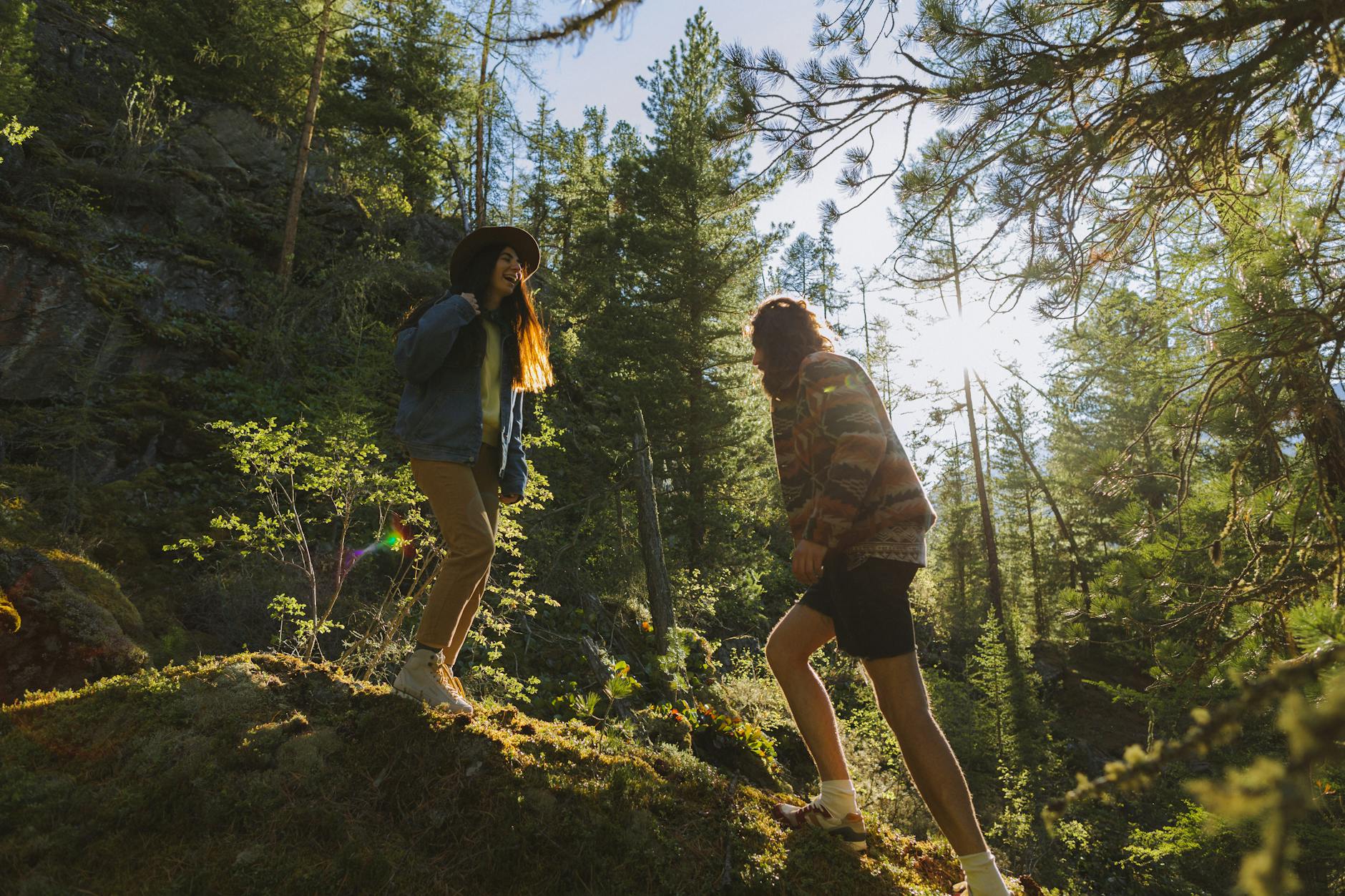Couple exploring a forest trail surrounded by sunlight and greenery, enjoying nature and adventure.