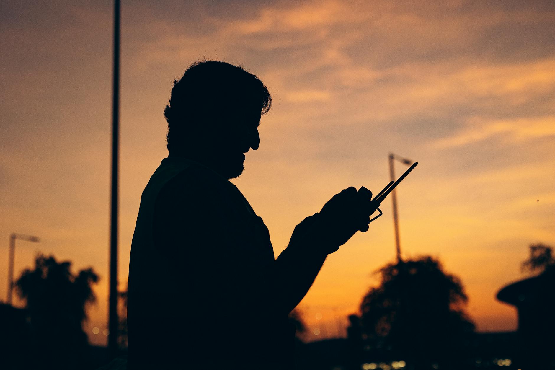Silhouette of a person holding a smartphone against a vibrant sunset in Abu Dhabi, UAE.