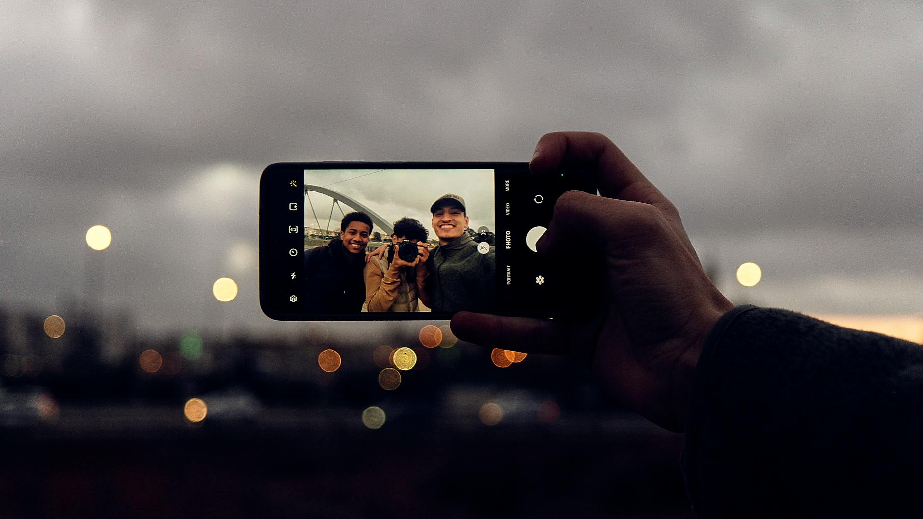 Friends taking a selfie outdoors with a smartphone showing vibrant bokeh background.