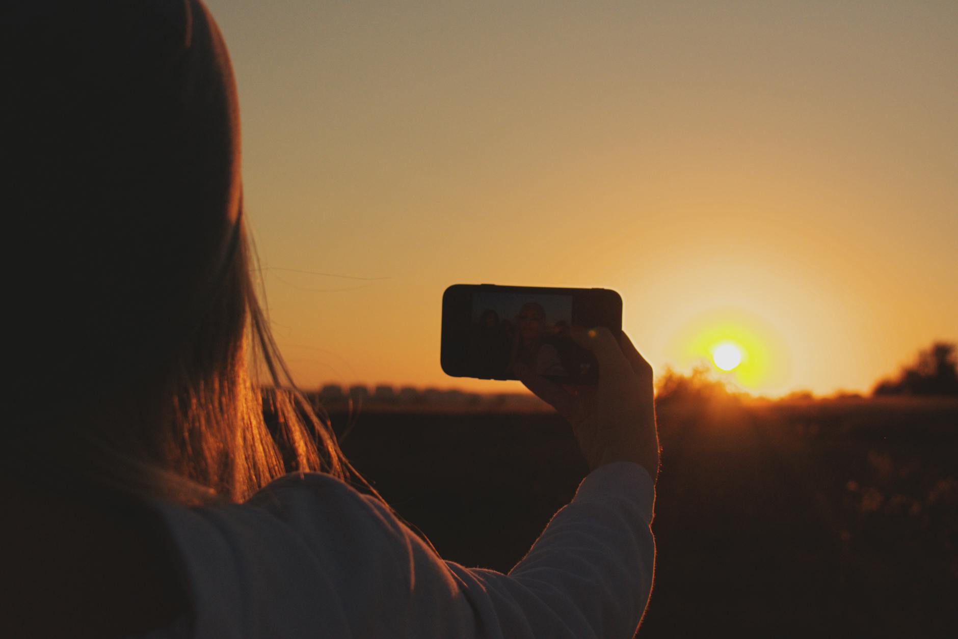 Silhouette of a person capturing a selfie against a vibrant sunset sky, creating a striking silhouette effect.