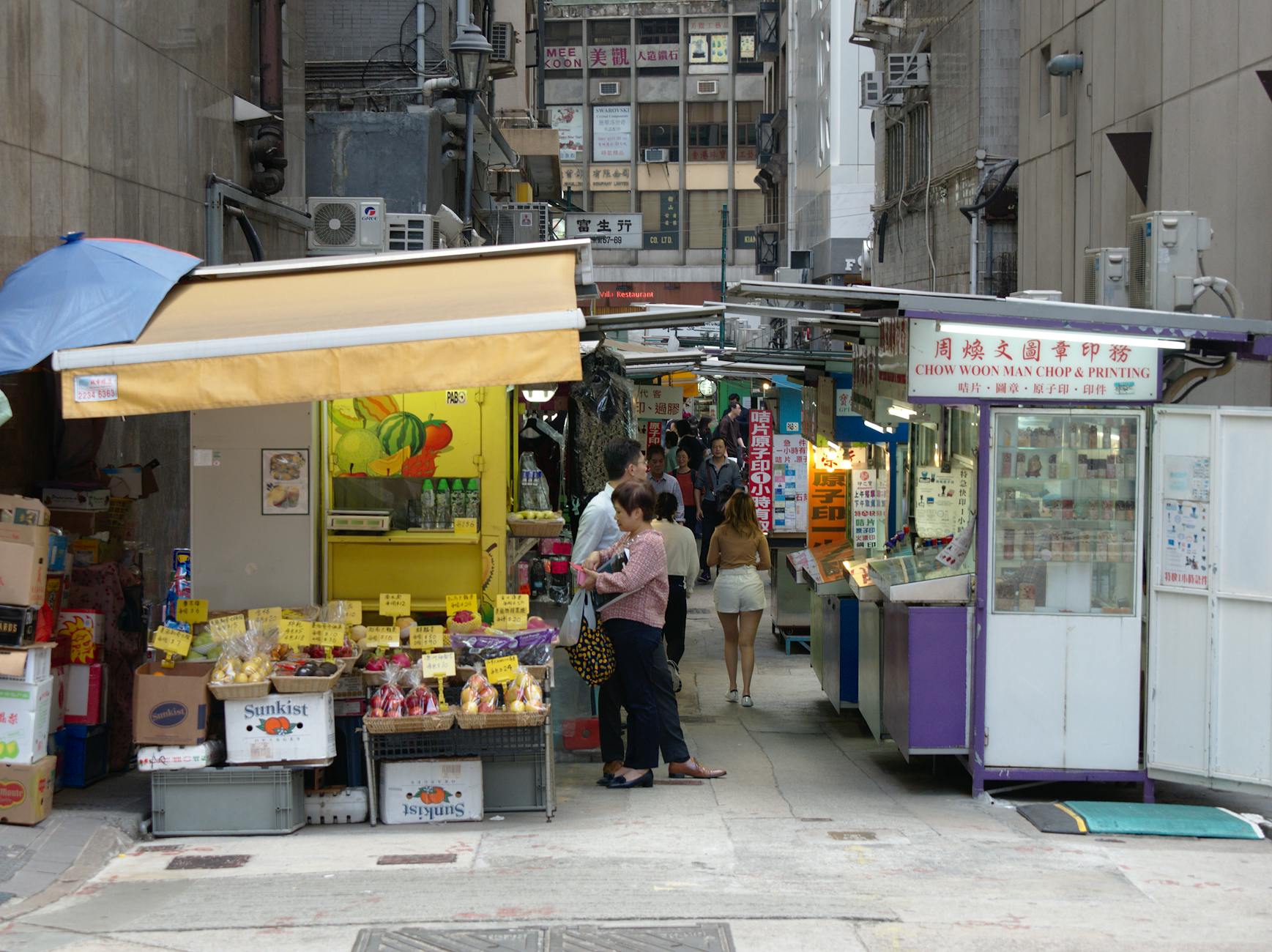 Busy street market with food stalls and people shopping in an urban alley.