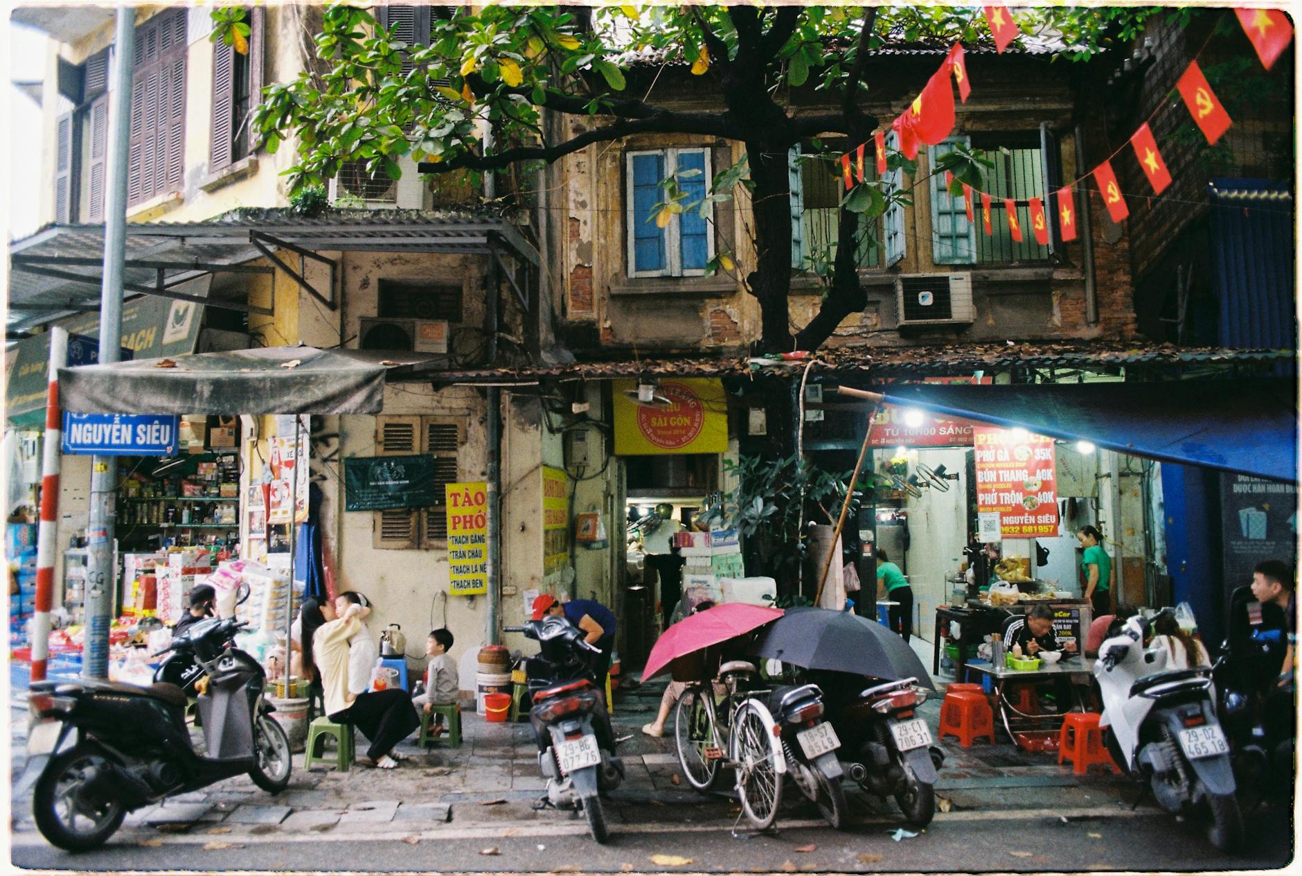 Vibrant street life in Hanoi, showing locals at a food stand with motorbikes and city life.