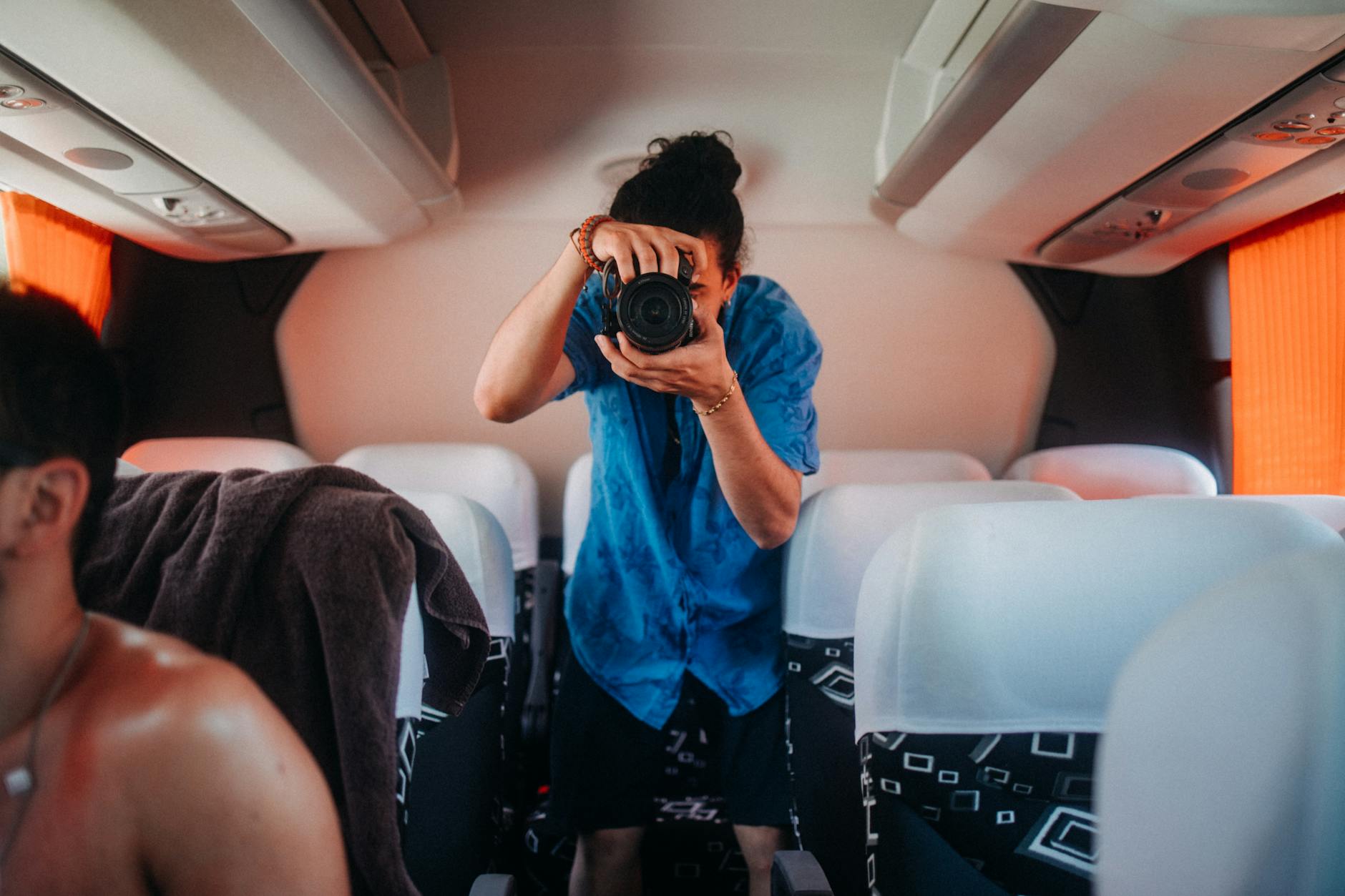 Casual man taking a photo with a camera inside a bus, capturing travel moments.