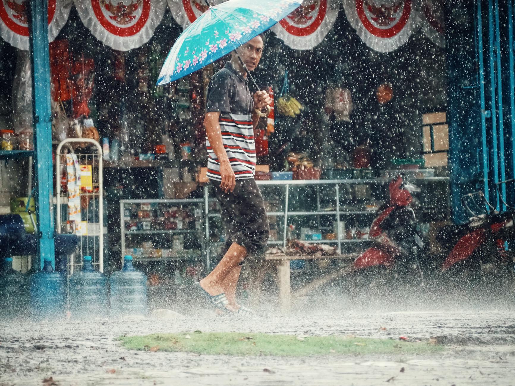 Street scene of a man with a blue umbrella navigating rain in West Java, Indonesia.
