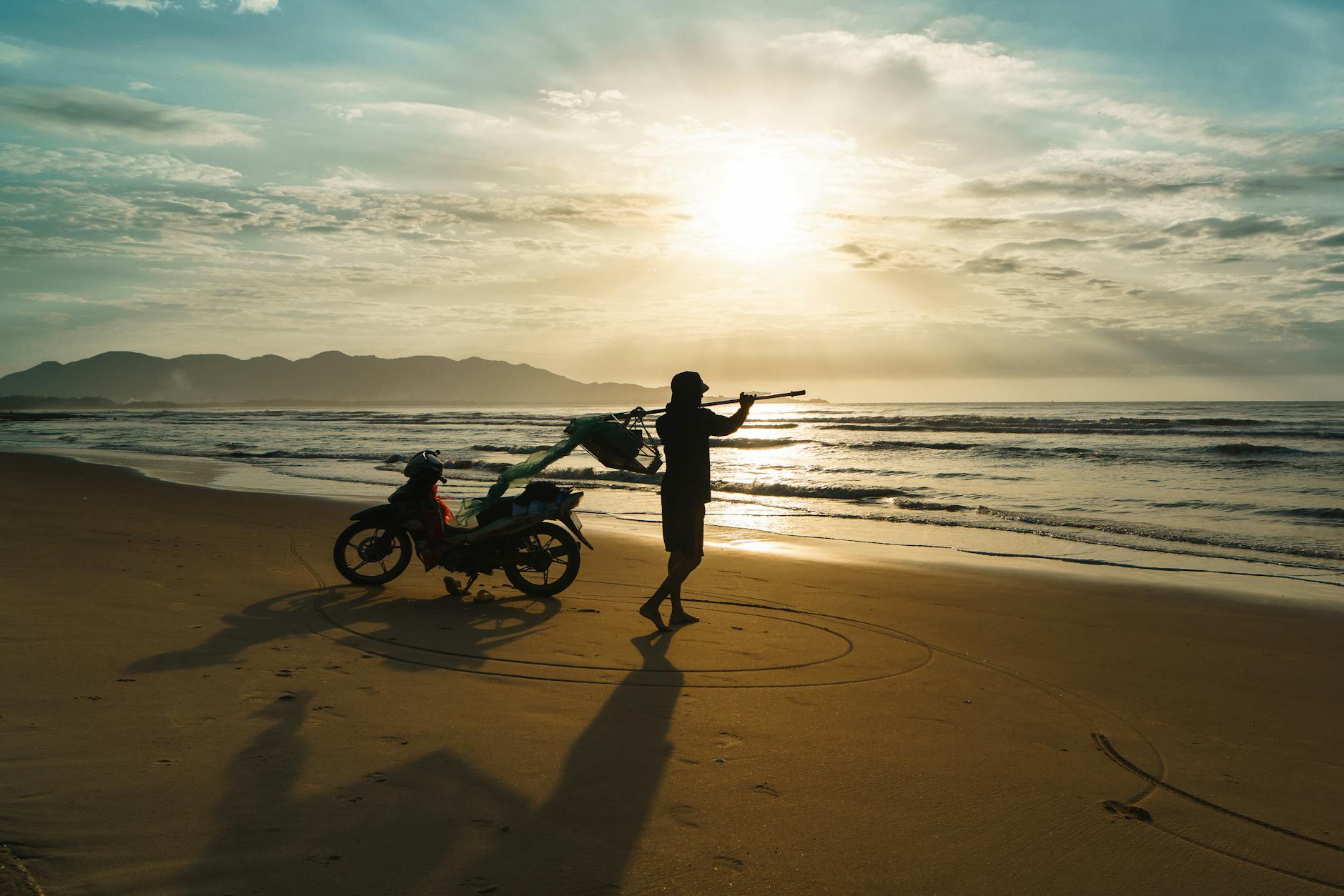 Silhouette of a fisherman with a motorcycle on Vũng Tàu Beach at sunrise, capturing daily life in Vietnam.
