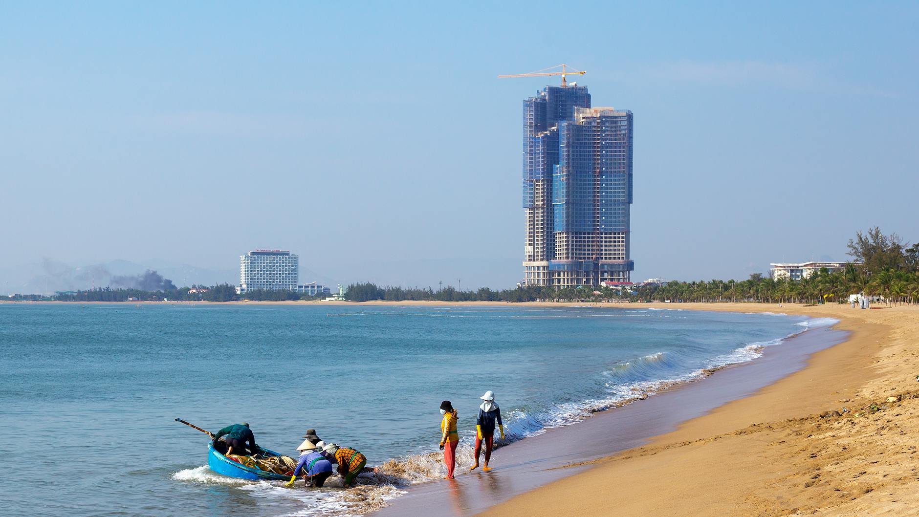 Fishermen on Ninh Thuận beach with a modern skyline backdrop, capturing the blend of tradition and development.